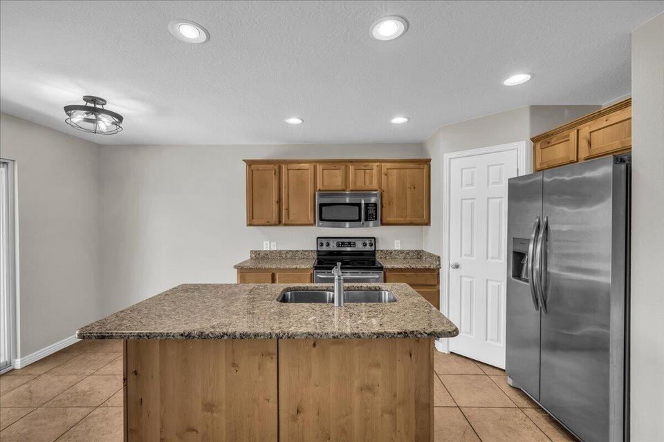 Kitchen featuring a central island with an undermount sink, granite countertops, wood-finish cabinetry, stainless steel appliances, and recessed lighting