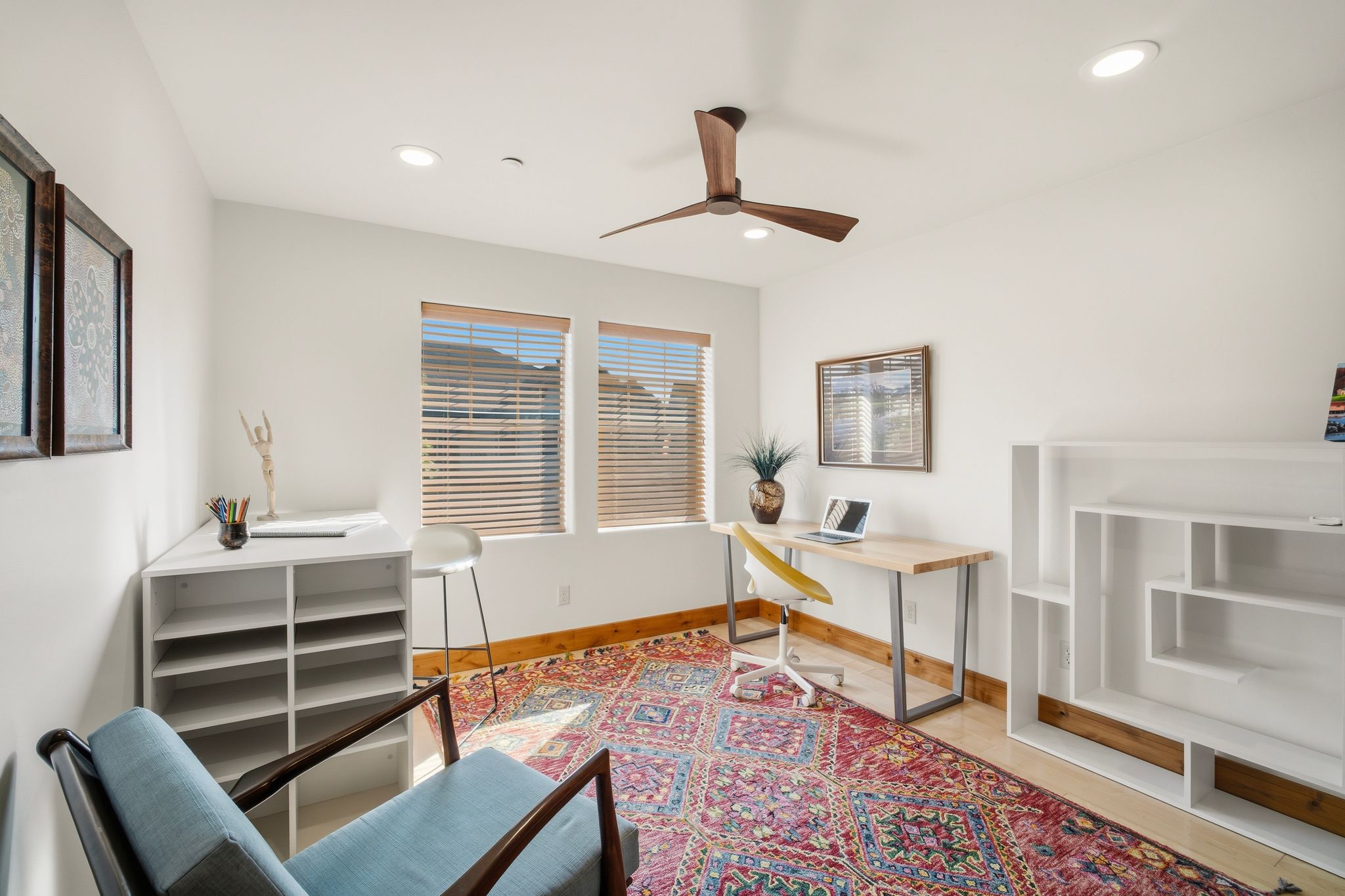 Recessed lighting illuminates this bright room featuring two windows with blinds, a ceiling fan with wood-finish blades, and wood baseboard trim