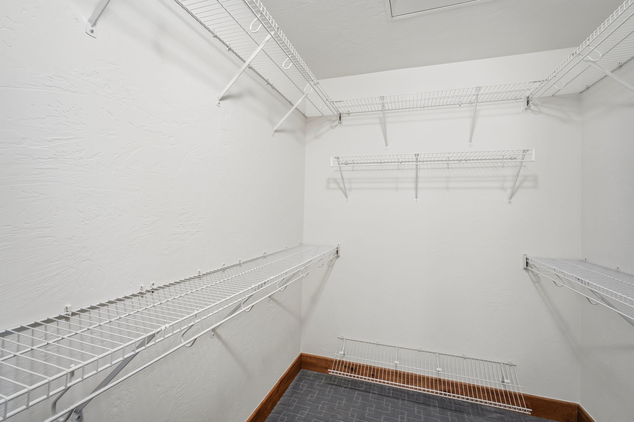 Walk-in closet featuring extensive wire shelving, white textured walls, and a durable tile-style flooring with perimeter wood-finish trim