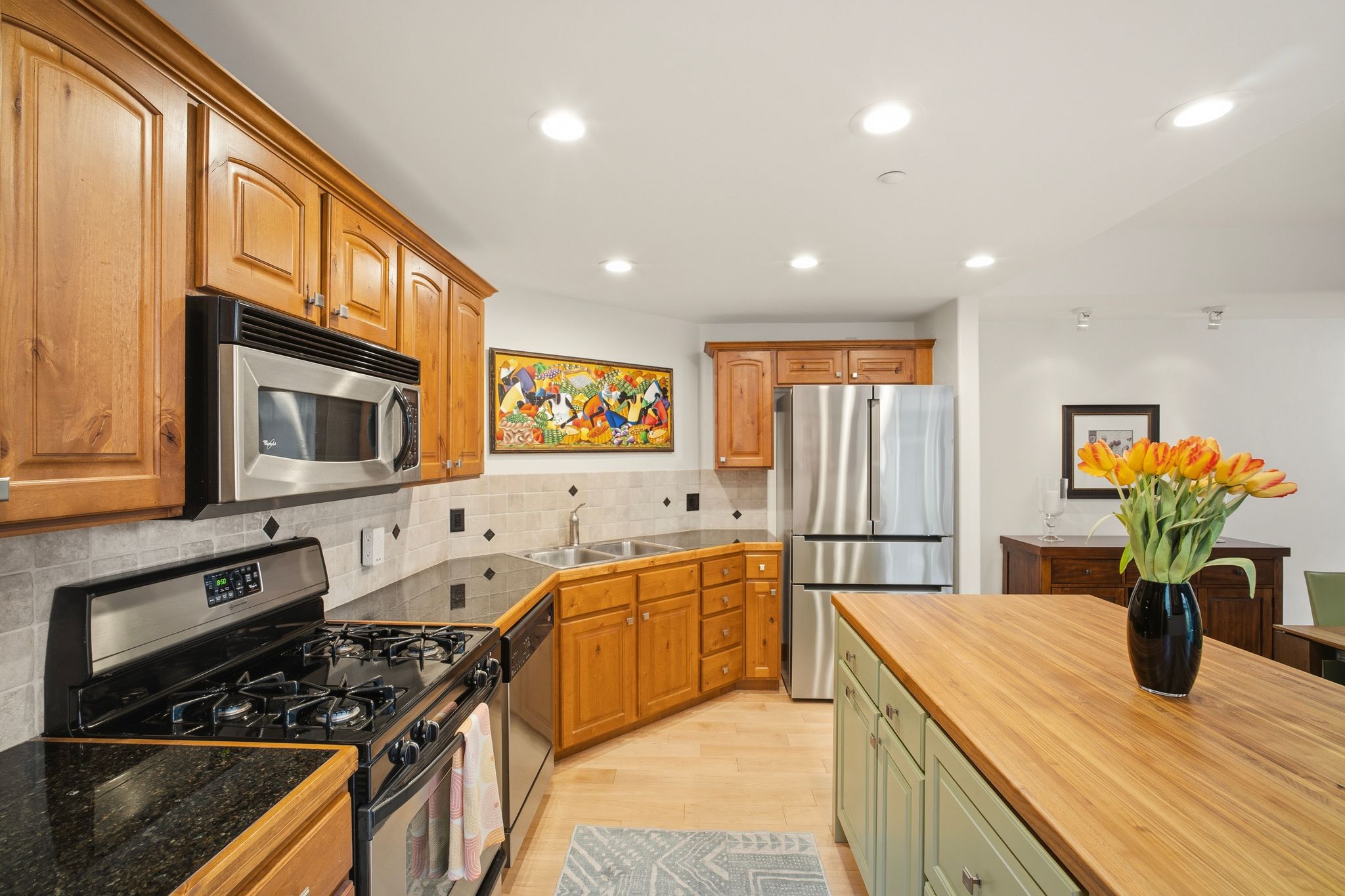 Kitchen featuring light wood cabinetry, stainless steel appliances, dark stone countertops, and a light-toned tile backsplash