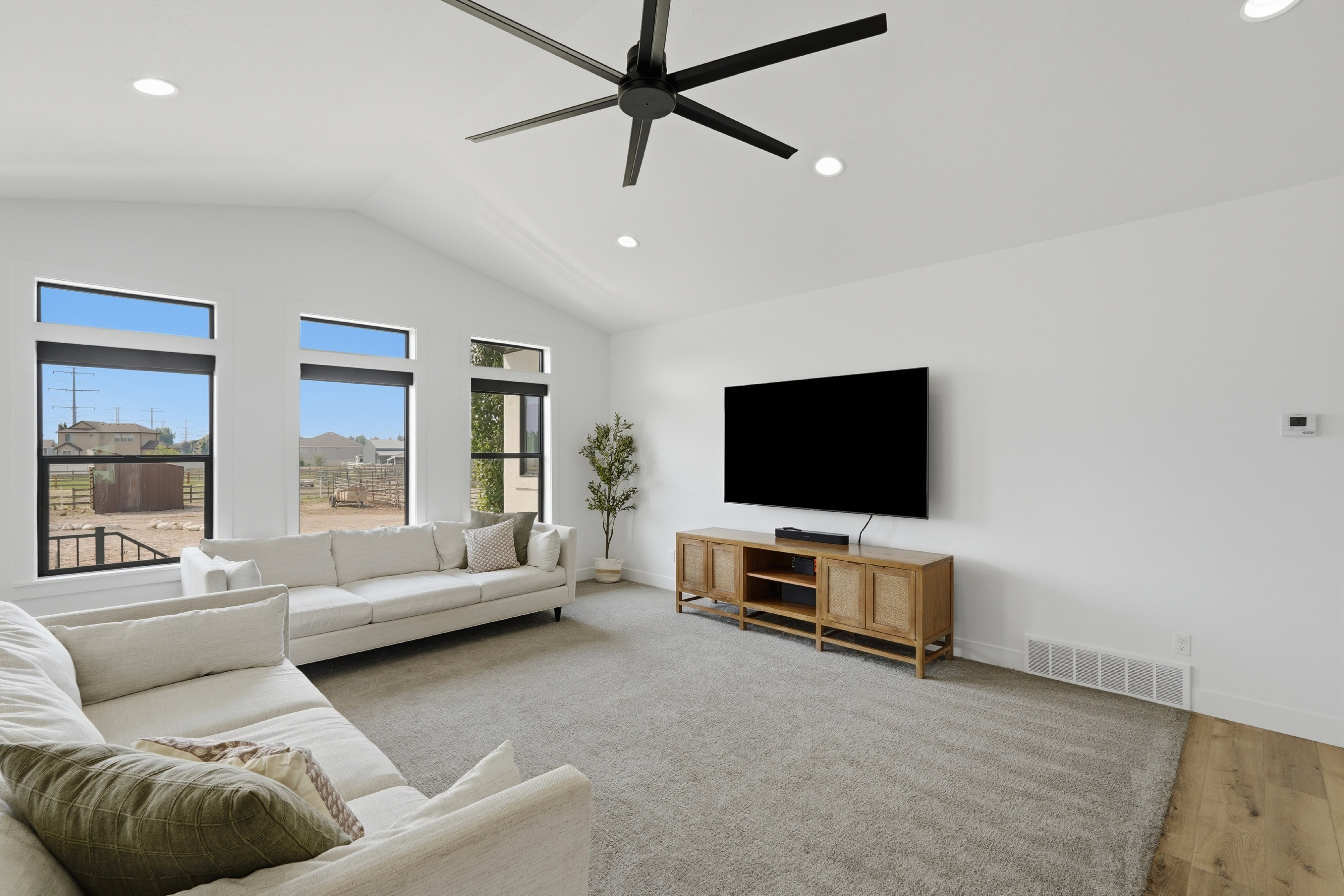 Spacious interior featuring vaulted ceilings, recessed lighting, a modern ceiling fan, and large windows with black trim