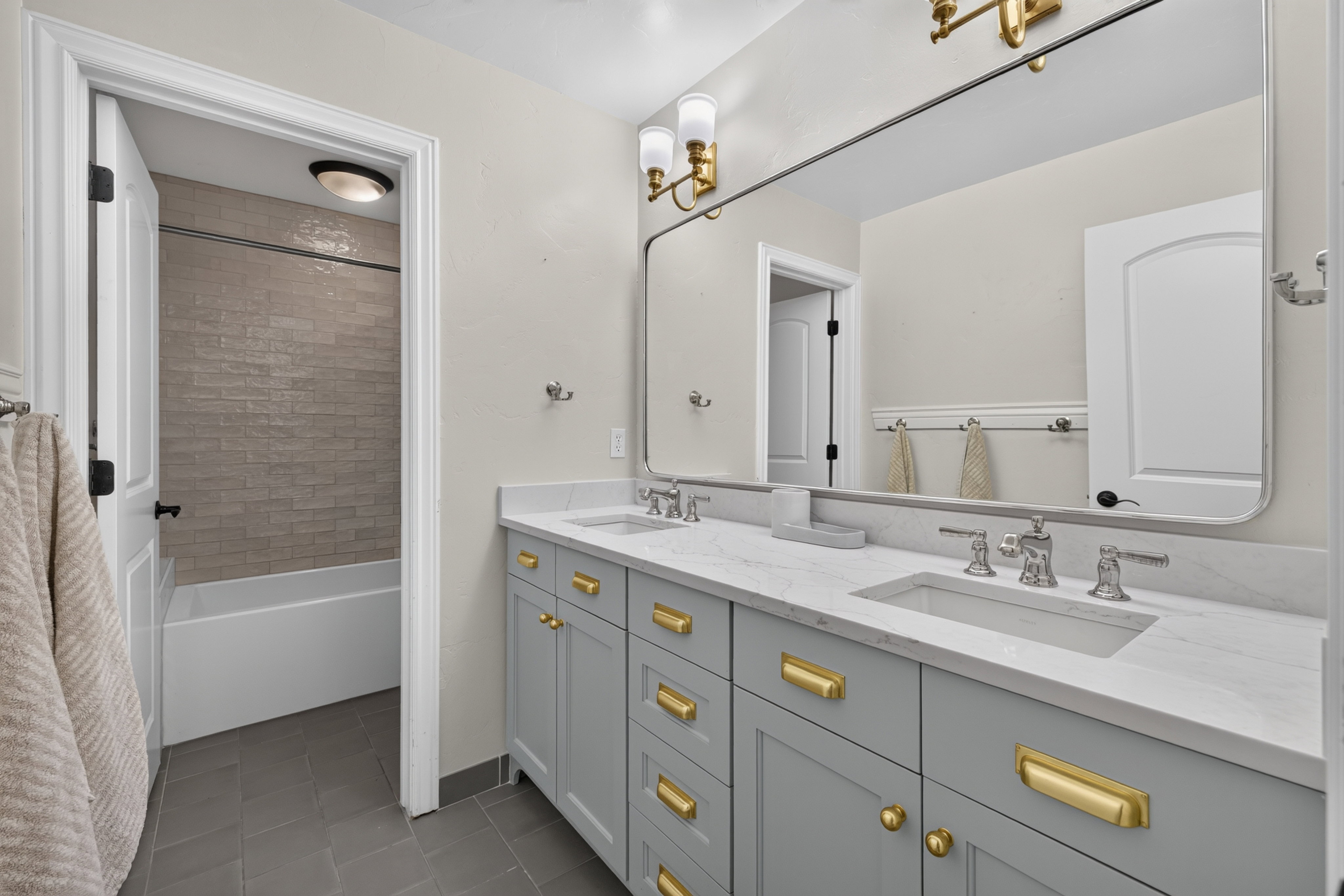 Double vanity featuring light gray cabinetry, gold-tone hardware, and an integrated marble-finish countertop with two undermount sinks