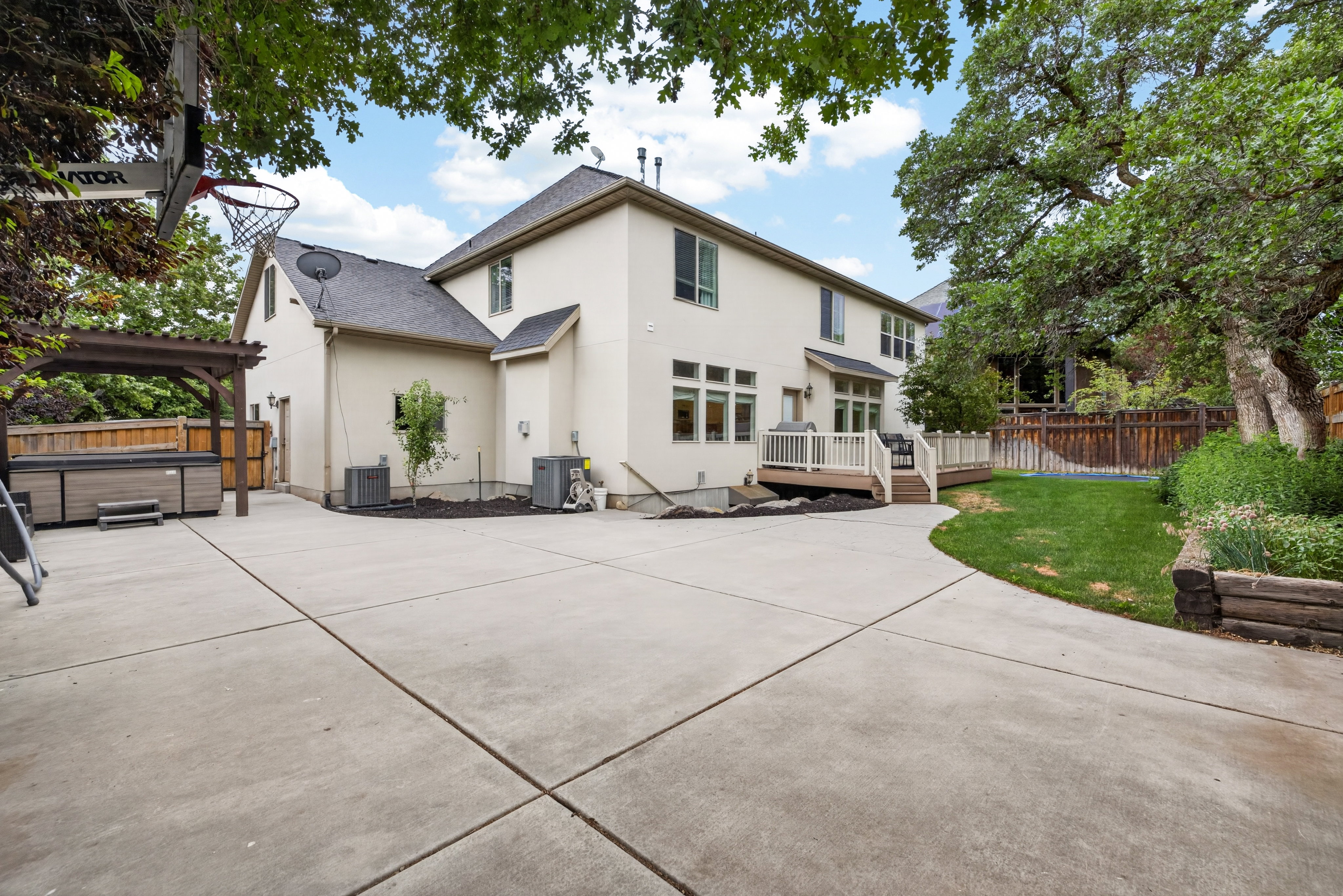 Rear exterior featuring a spacious concrete patio, a multi-level deck with white railings, and a hot tub beneath a wooden pergola