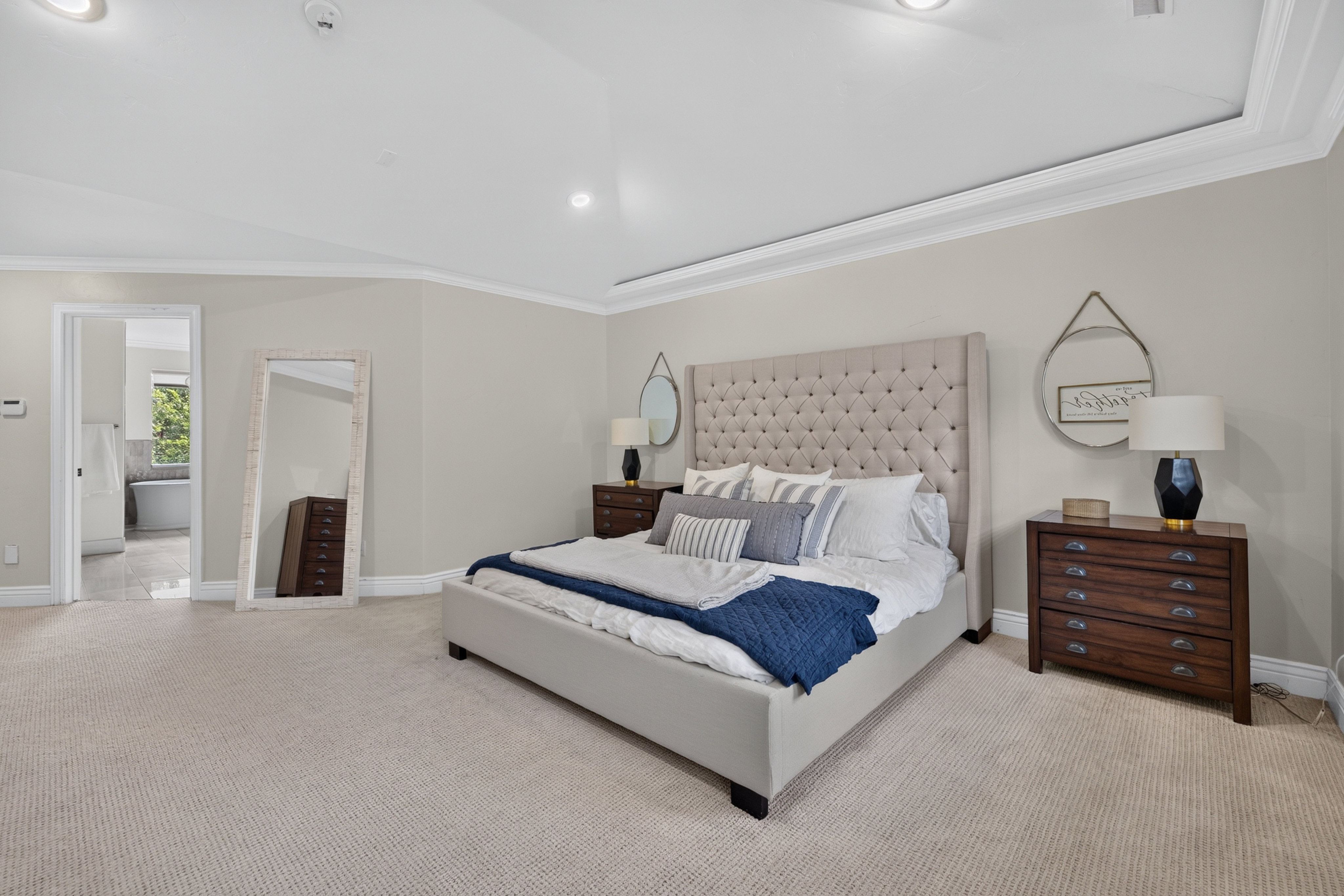Spacious bedroom featuring neutral carpeting, tray ceiling with recessed lighting, and crown molding