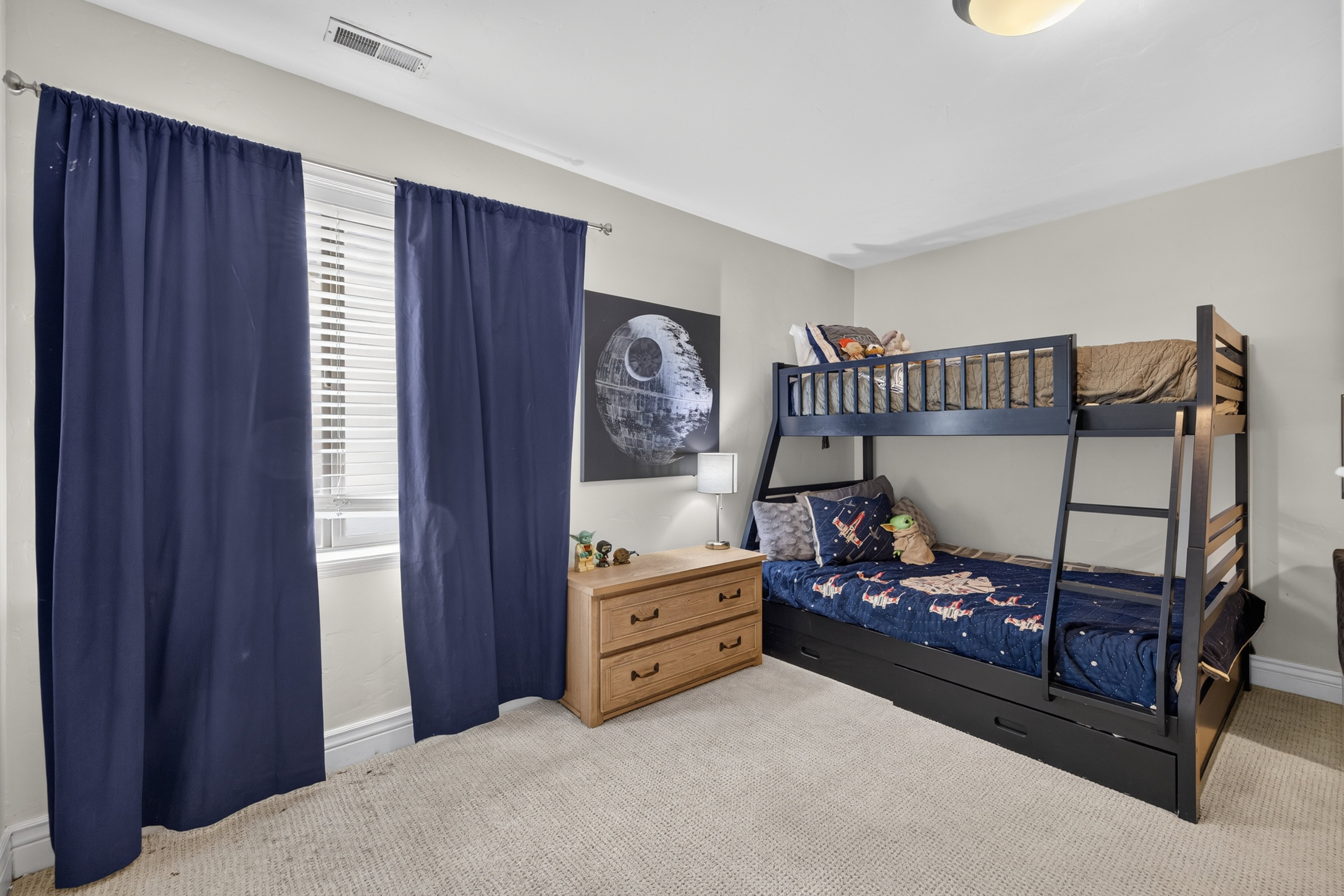 Carpeted room featuring a window with horizontal blinds and full-length blue drapes, a bunk bed with an integrated ladder, and a flush-mount ceiling light fixture