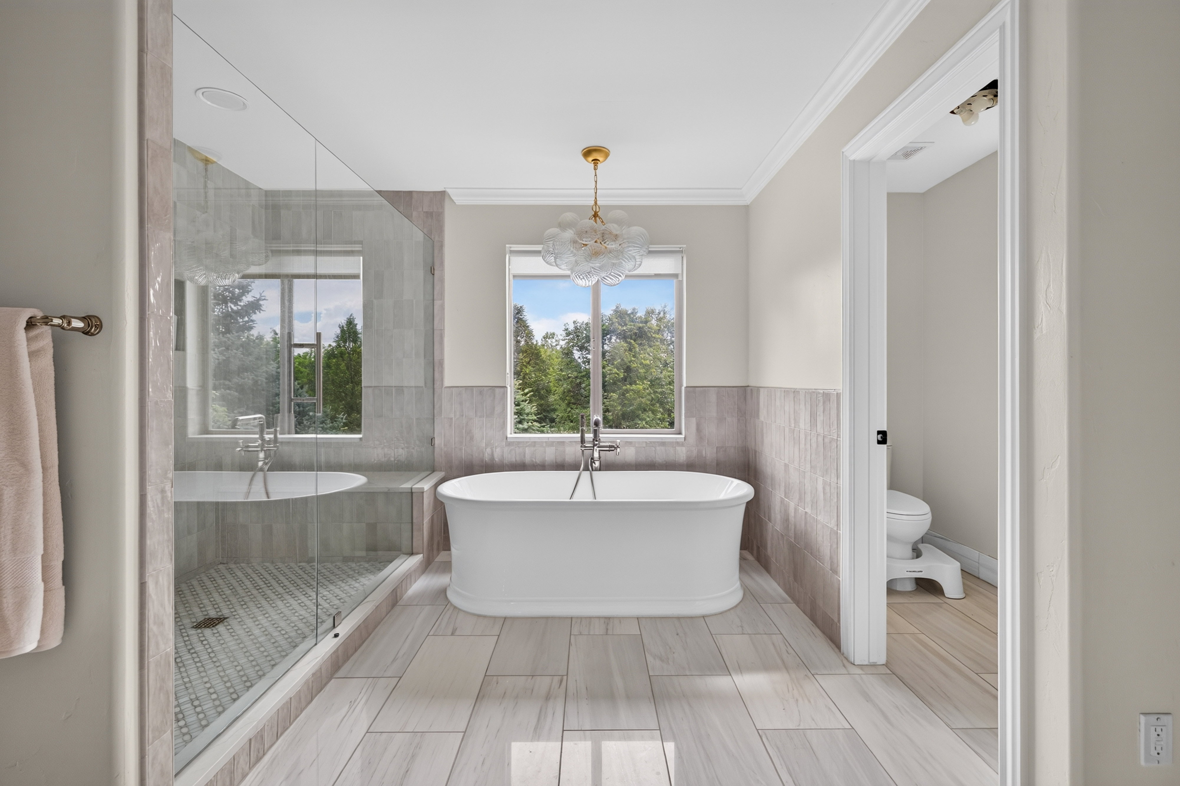 Freestanding soaking tub with a modern chandelier, oversized glass-enclosed shower, wood-finish flooring, and crown molding