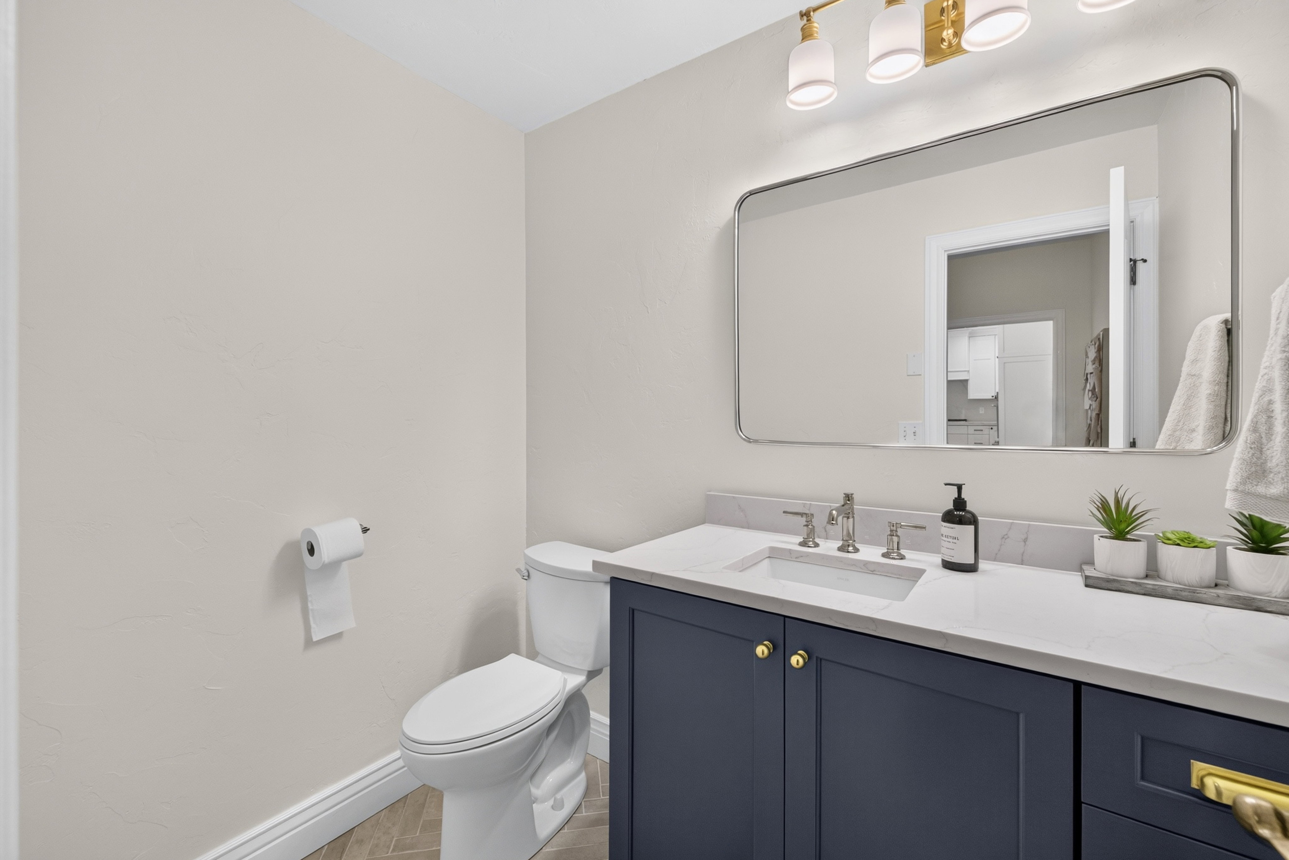 Bathroom vanity featuring a quartz countertop with an undermount sink, brass hardware, and a dark blue cabinet