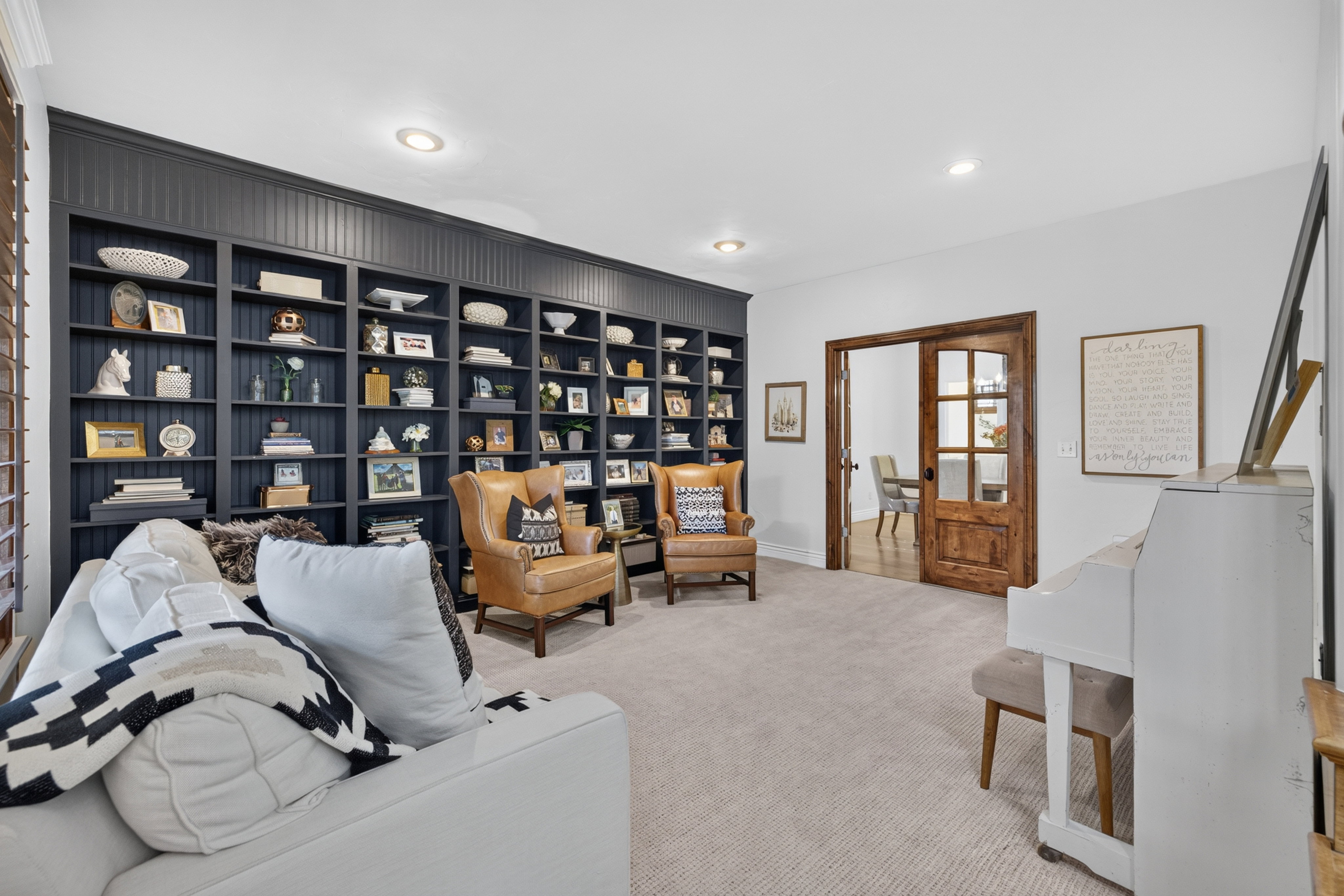 Spacious room featuring a full wall of built-in shelving with beadboard detailing, recessed lighting, and light-toned carpeting