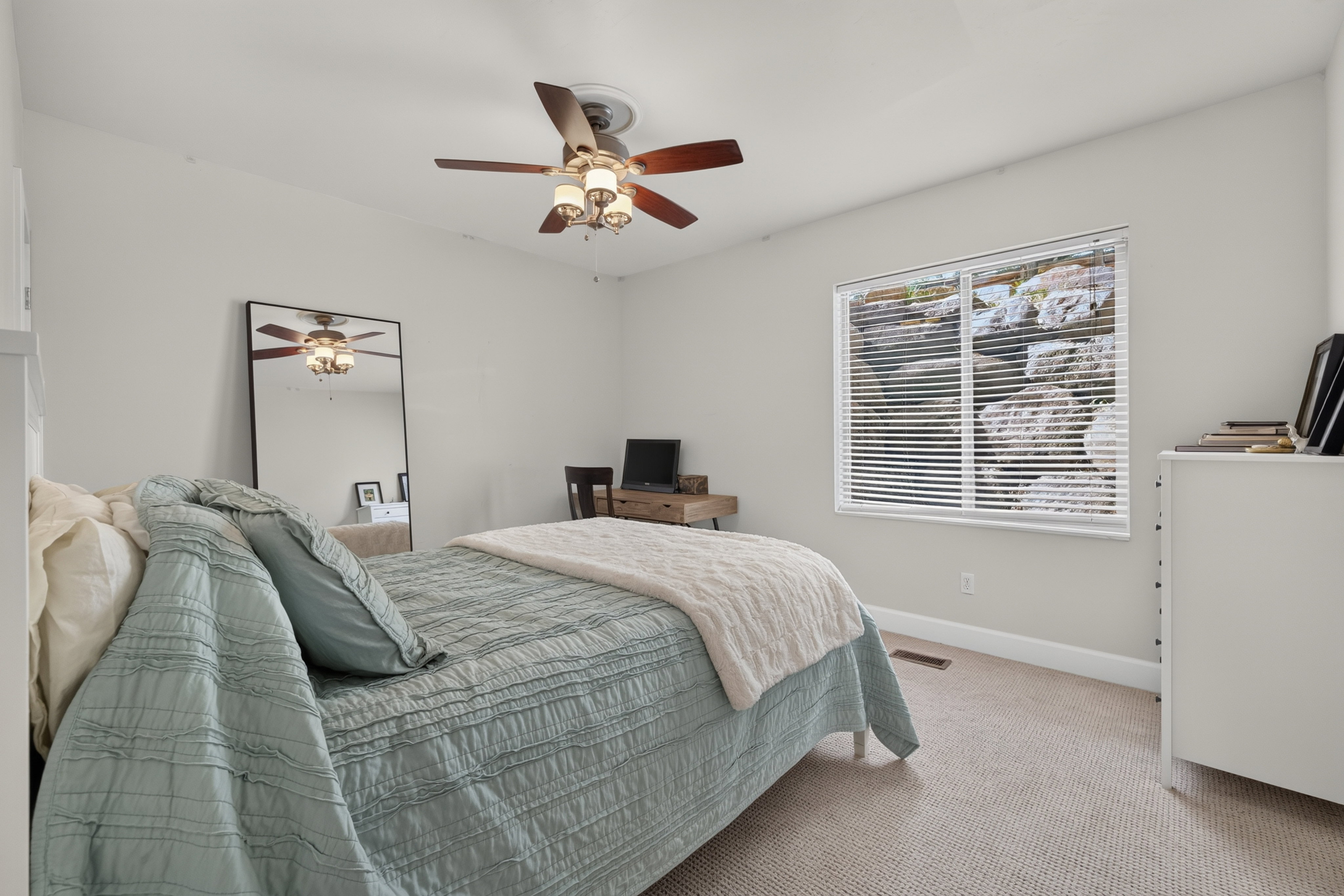 Neutral-toned bedroom featuring a ceiling fan with integrated lighting, a window with horizontal blinds, and light-colored carpeting