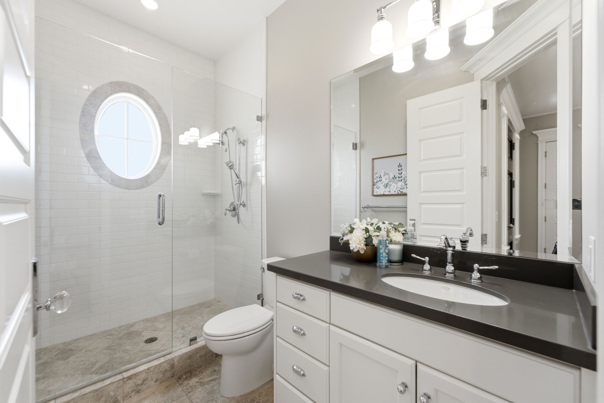 Contemporary bathroom featuring a frameless glass shower enclosure with a unique circular window and white subway tile surround