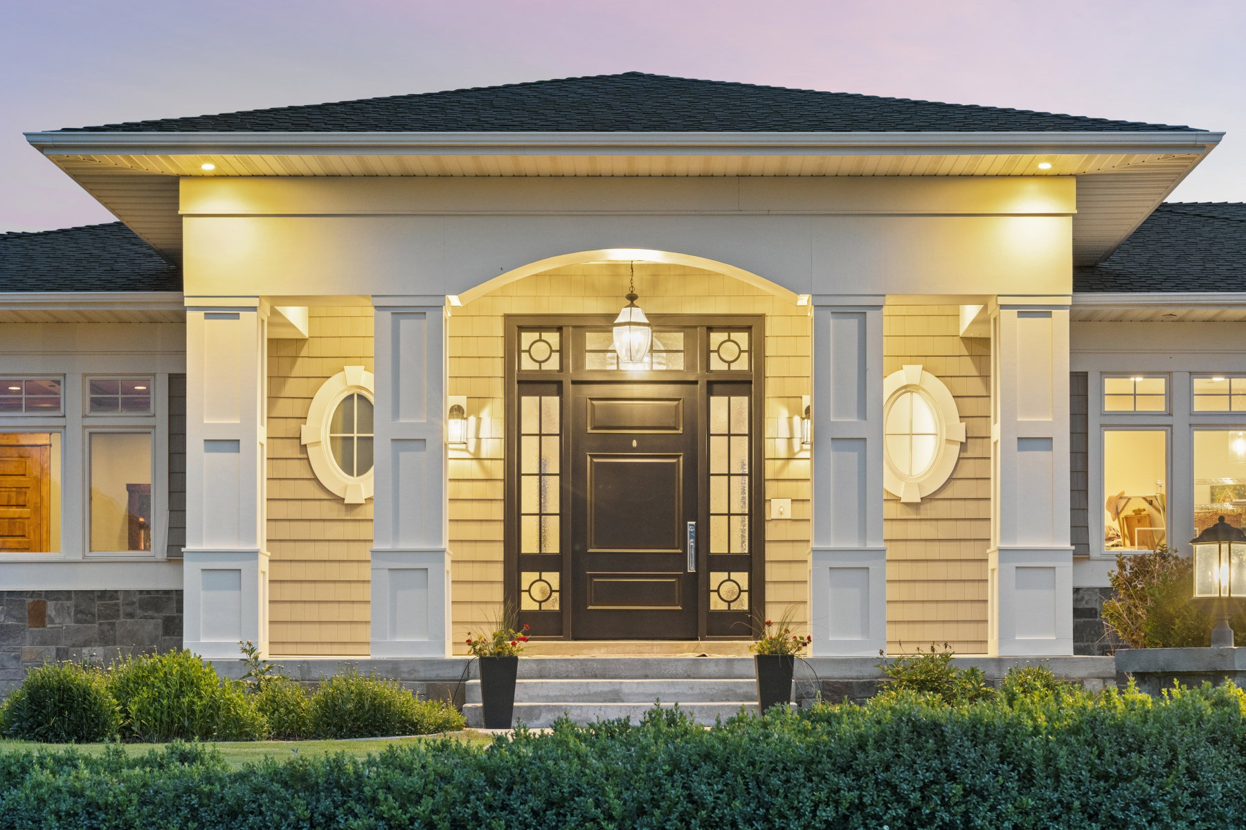 Arched entryway featuring a dark paneled door with glass inserts, flanked by decorative oval windows and sconce lighting