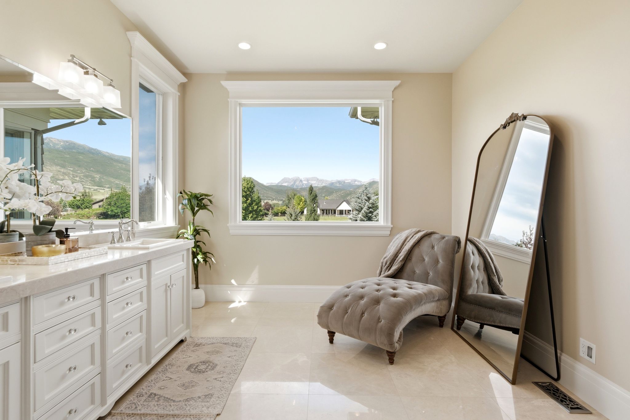 Light-filled bathroom featuring a double vanity with stone countertop, polished chrome fixtures, and white cabinetry