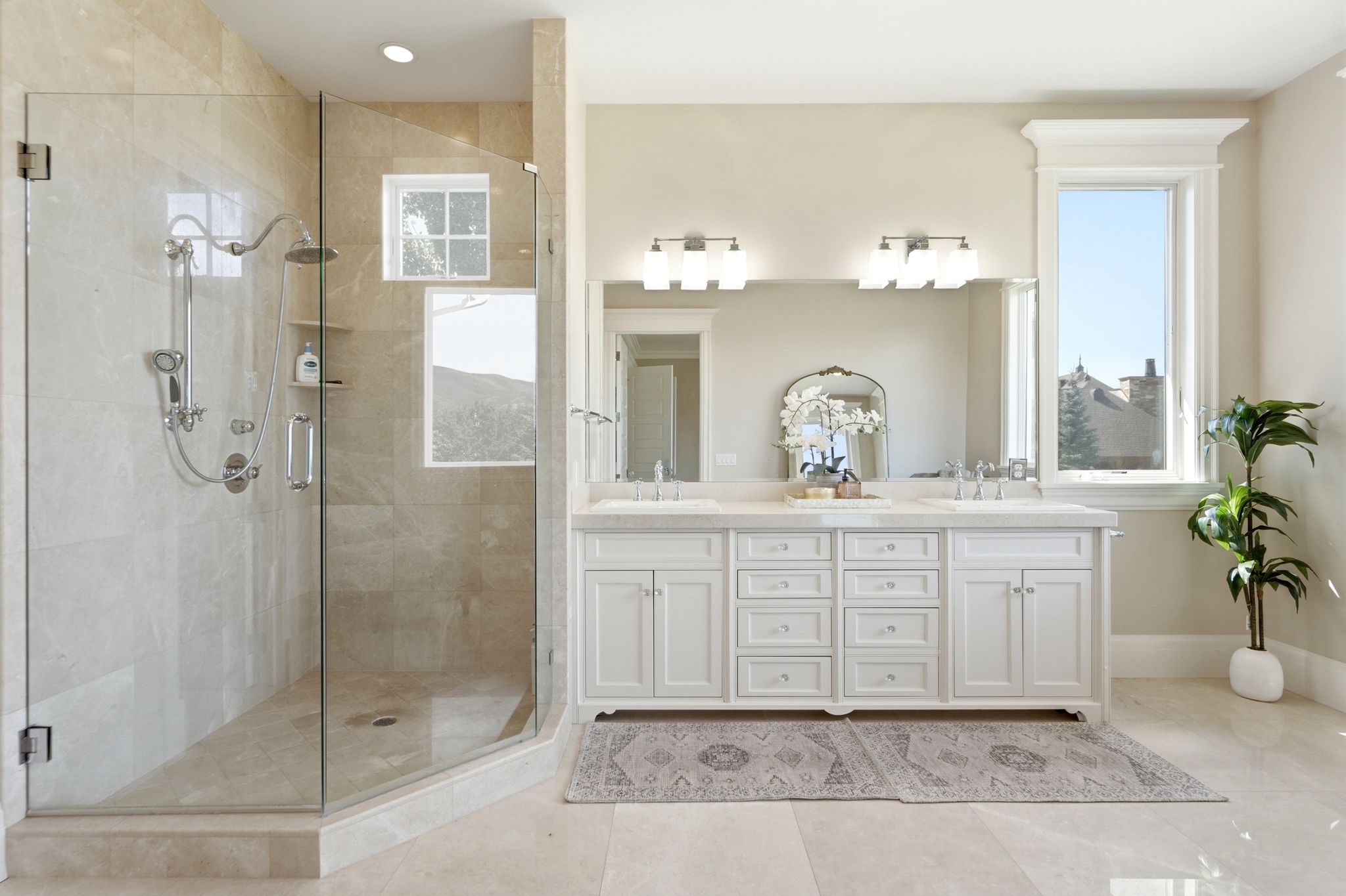 Spacious bathroom featuring a glass-enclosed shower with multiple showerheads, a dual vanity with white cabinetry and undermount sinks, and light-toned tile flooring