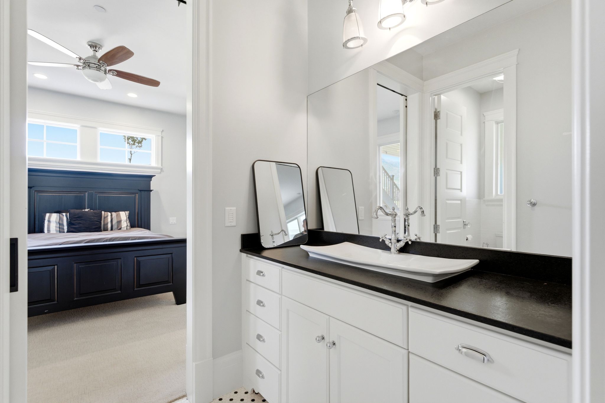 Vanity featuring a white vessel sink, polished chrome faucet, and dark countertop, complemented by white cabinetry with polished chrome hardware