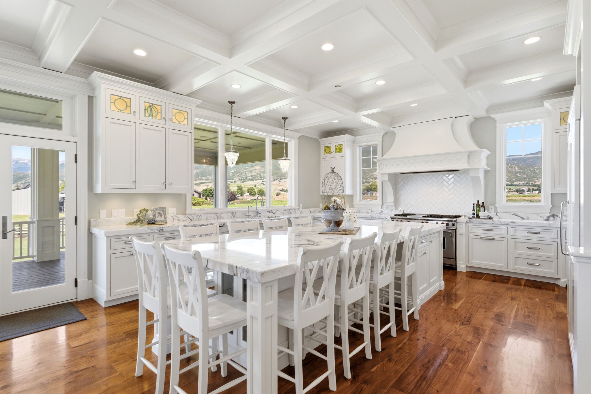 Gourmet kitchen featuring a large central island with seating, white cabinetry, polished stone countertops, coffered ceilings, and wood-finish flooring