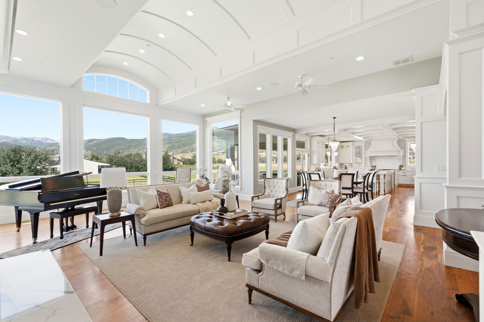 Spacious living area featuring expansive windows, natural wood flooring, a coffered ceiling with recessed lighting, and a neutral color palette