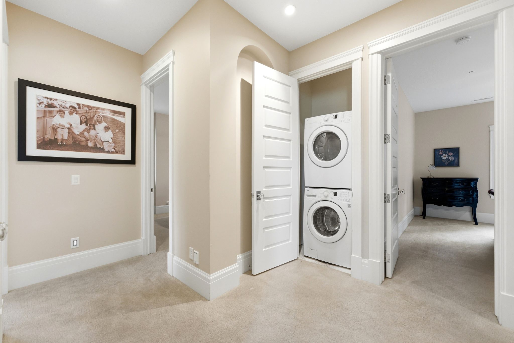 Integrated stacked washer and dryer unit within a dedicated closet space, featuring panel-style doors and overhead recessed lighting