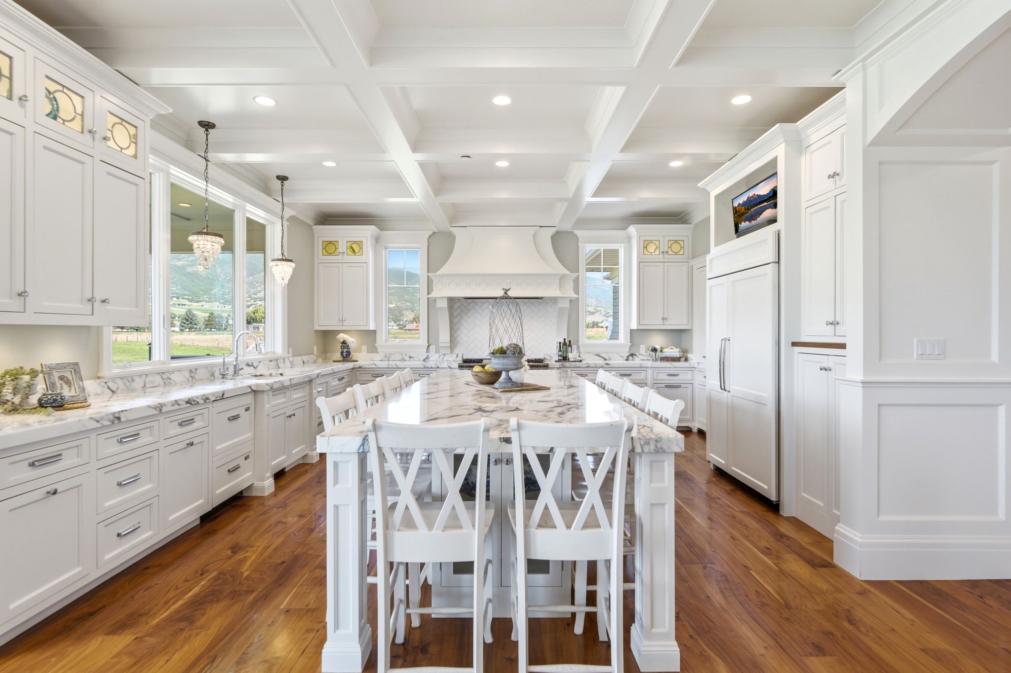 Gourmet kitchen featuring a large central island with seating, extensive white cabinetry, marbled countertops, and wood-finish flooring