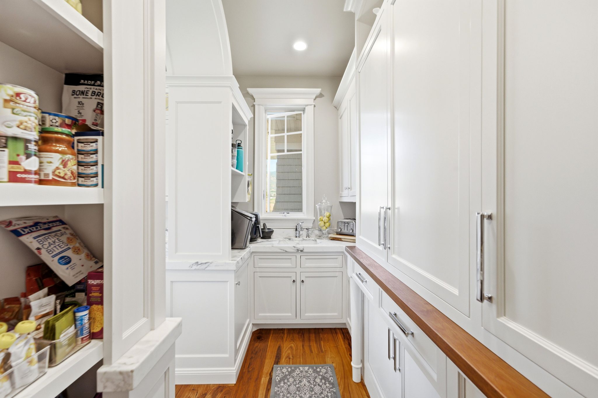 Walk-in pantry with extensive built-in shelving, white cabinetry, a built-in sink, and wood-finish flooring