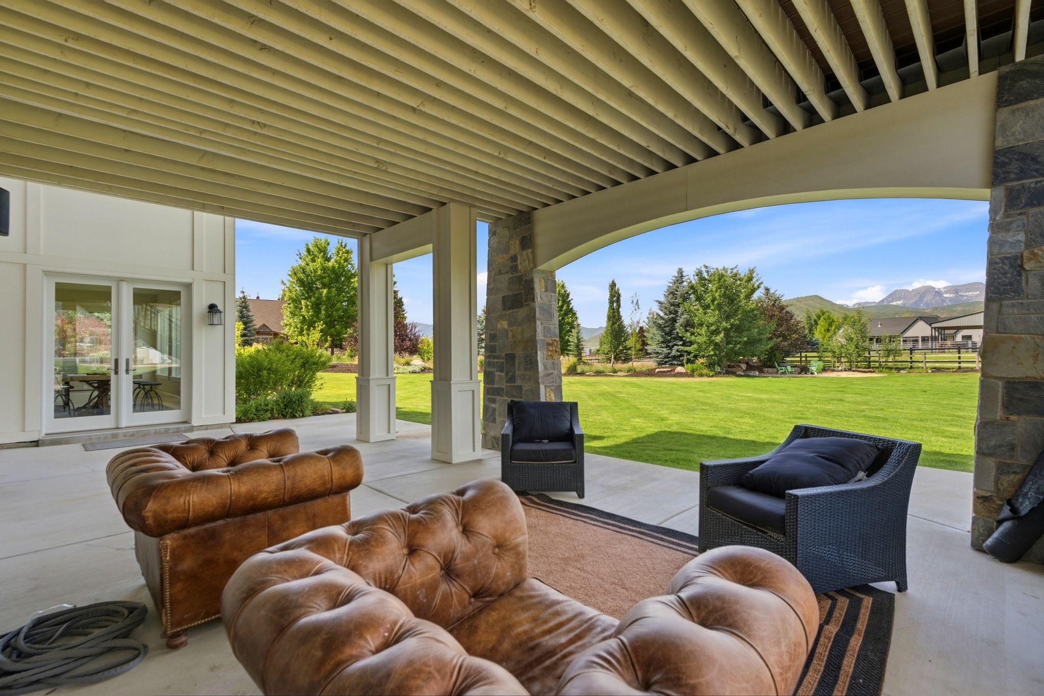 Expansive covered patio featuring a concrete floor, stone-clad structural columns, and a tongue-and-groove ceiling