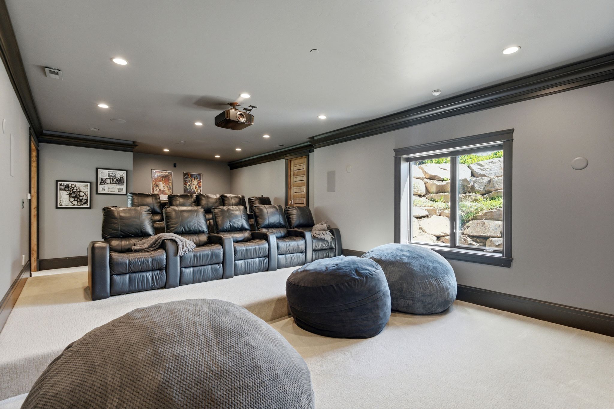 Dedicated home theater featuring tiered seating, recessed lighting, ceiling-mounted projector, and a visible window with rock landscaping outside
