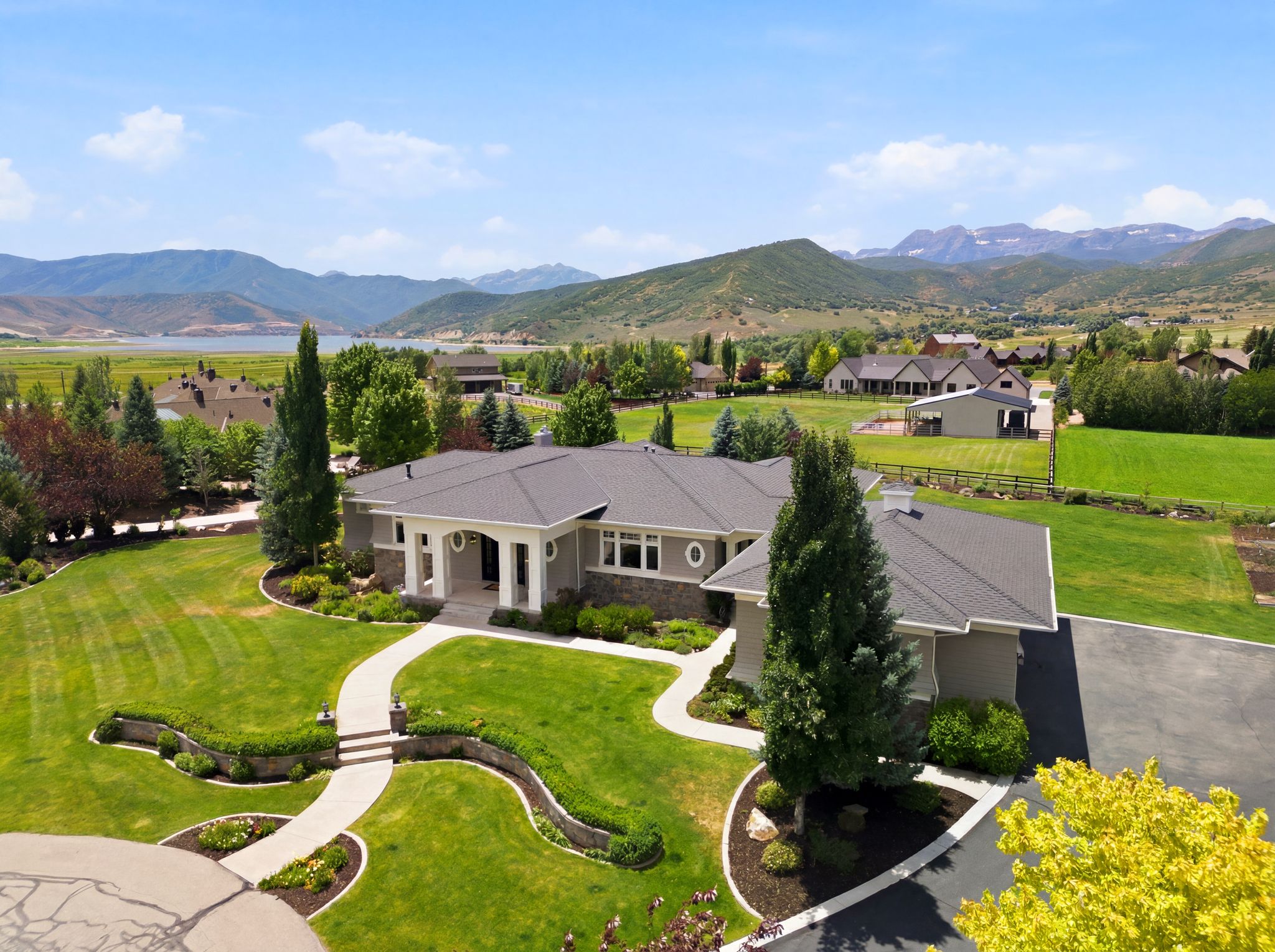 Expansive property featuring a meticulously landscaped lawn, mature trees, and a curved paved driveway