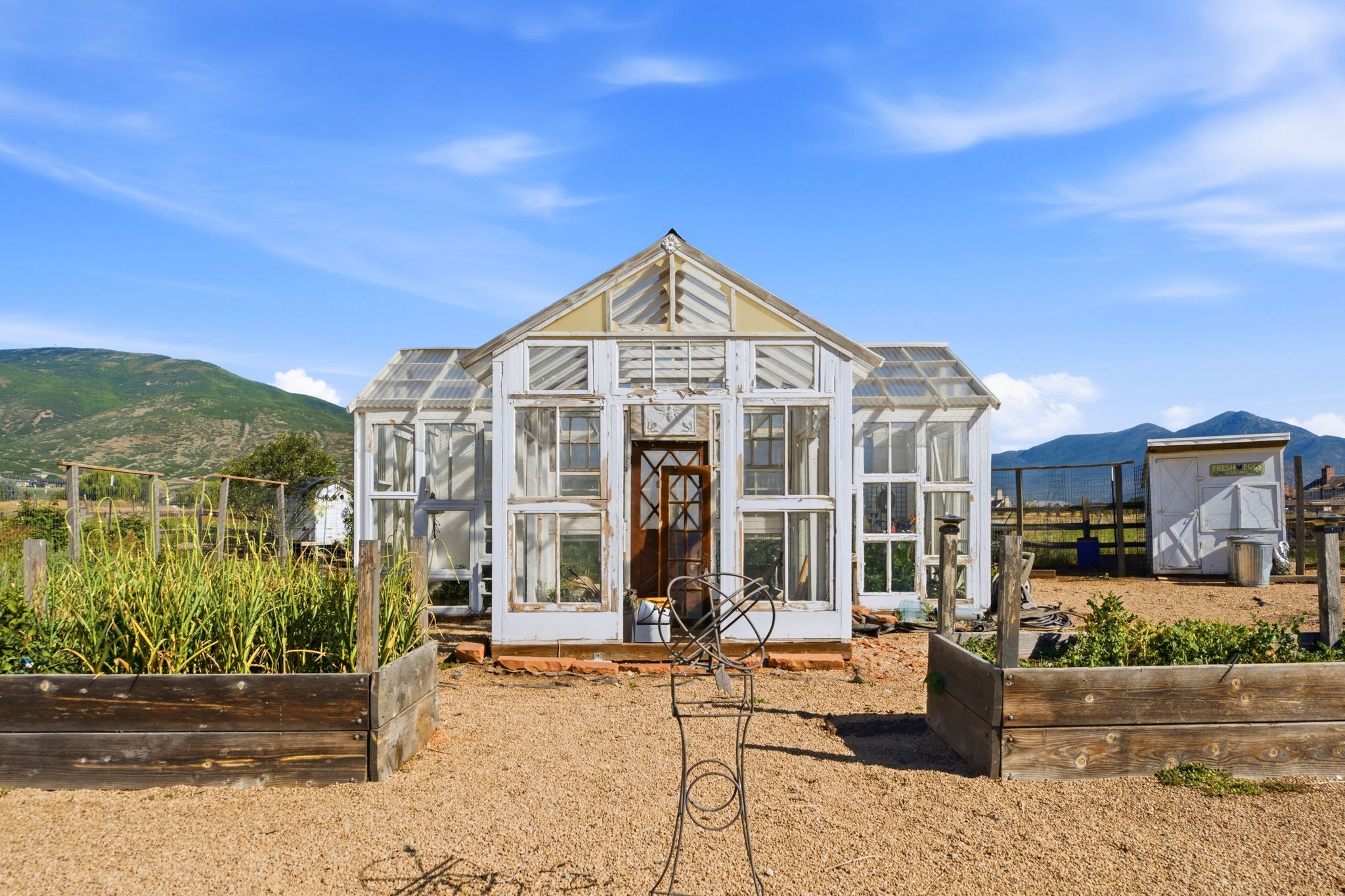 White-framed greenhouse with a wood-panel door, set on a gravel-covered ground