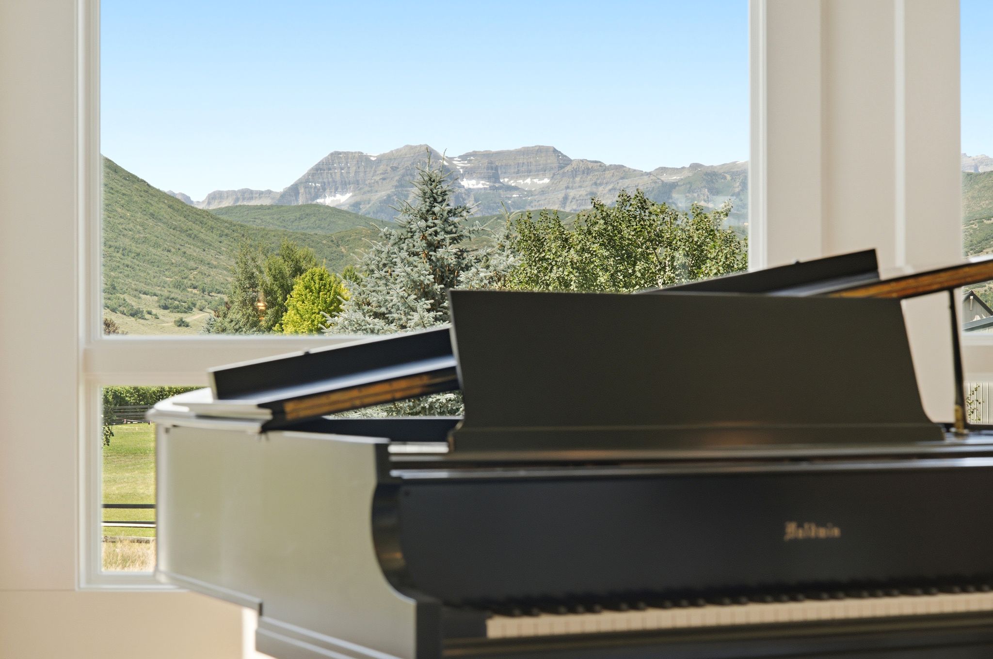 Floor-to-ceiling windows frame a mountain backdrop and lush green landscape