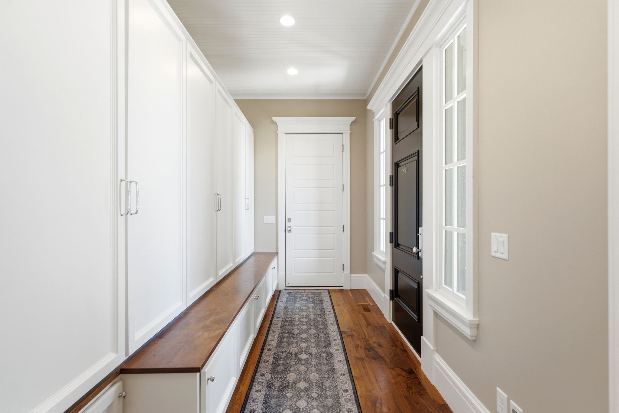 Entryway with wood-finish flooring, a full wall of built-in white cabinetry, and a dark paneled door with sidelight windows
