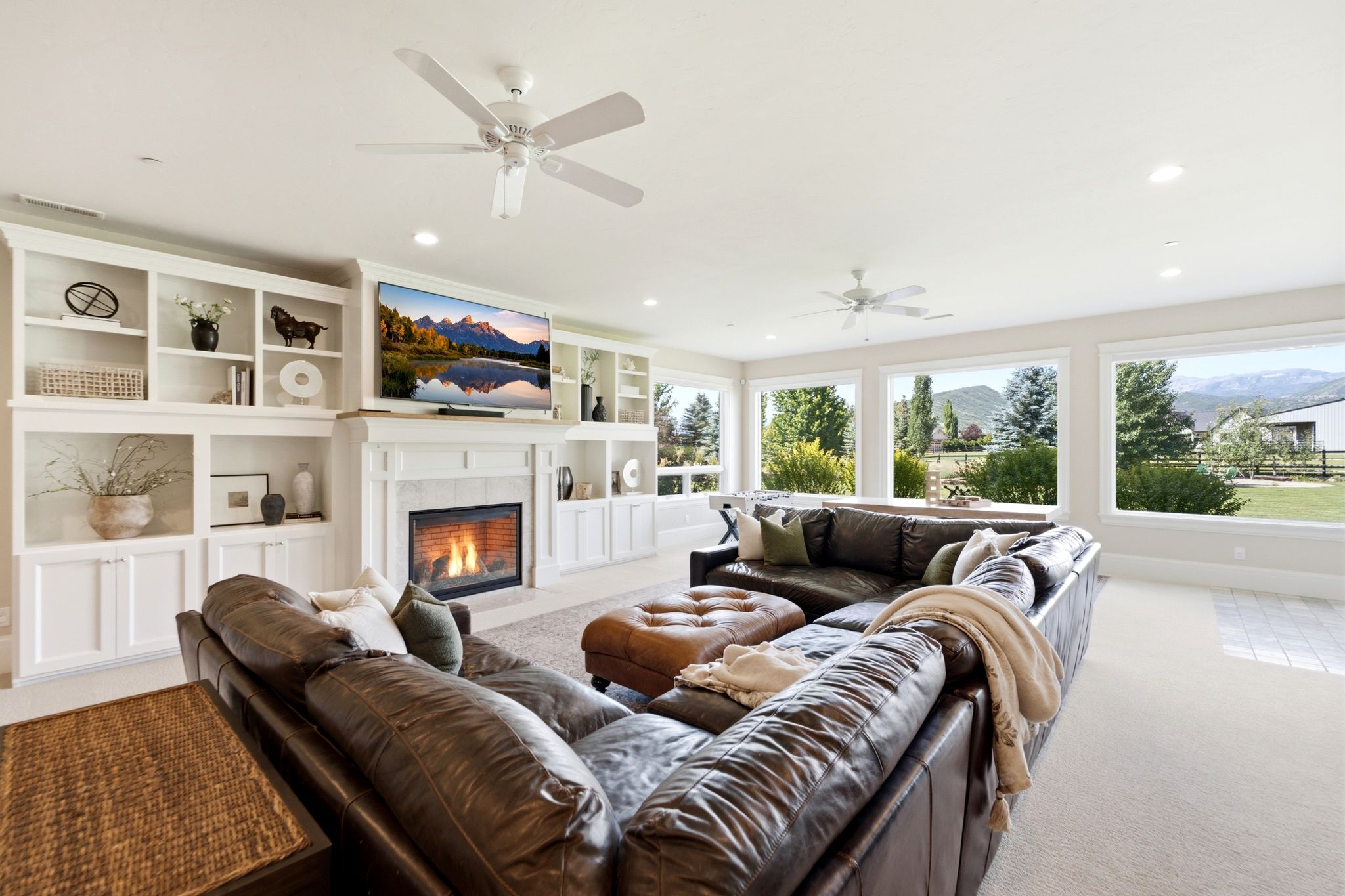 Spacious living area featuring extensive built-in shelving, a central fireplace with a mantel, and multiple large windows overlooking a distant mountain landscape