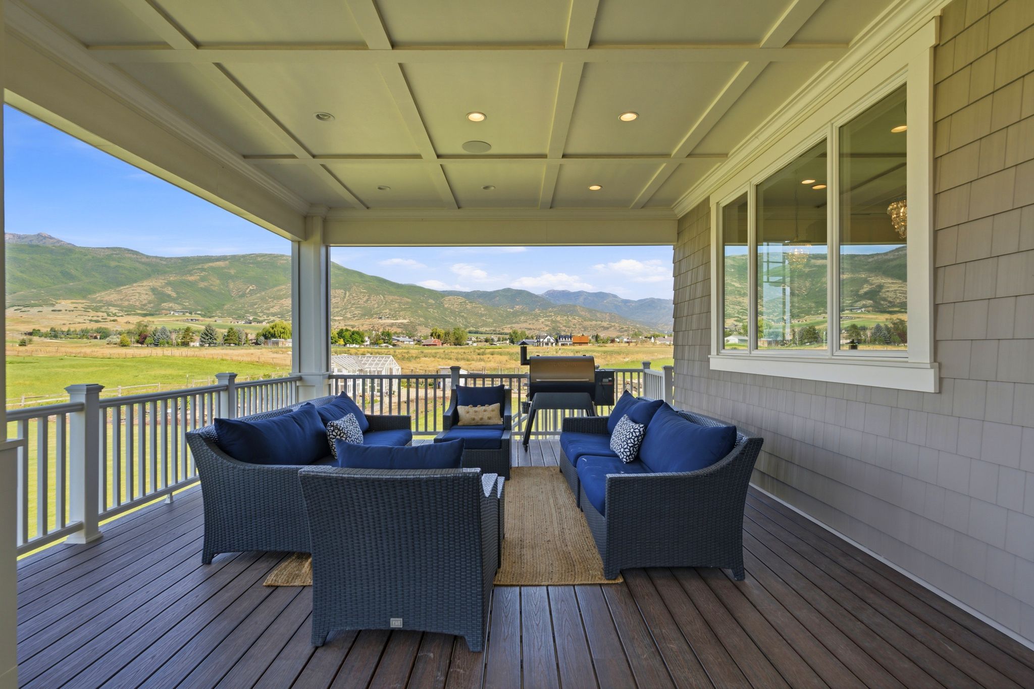 Covered outdoor patio with mountain scenery, featuring a coffered ceiling with recessed lighting, composite decking, and shaker siding