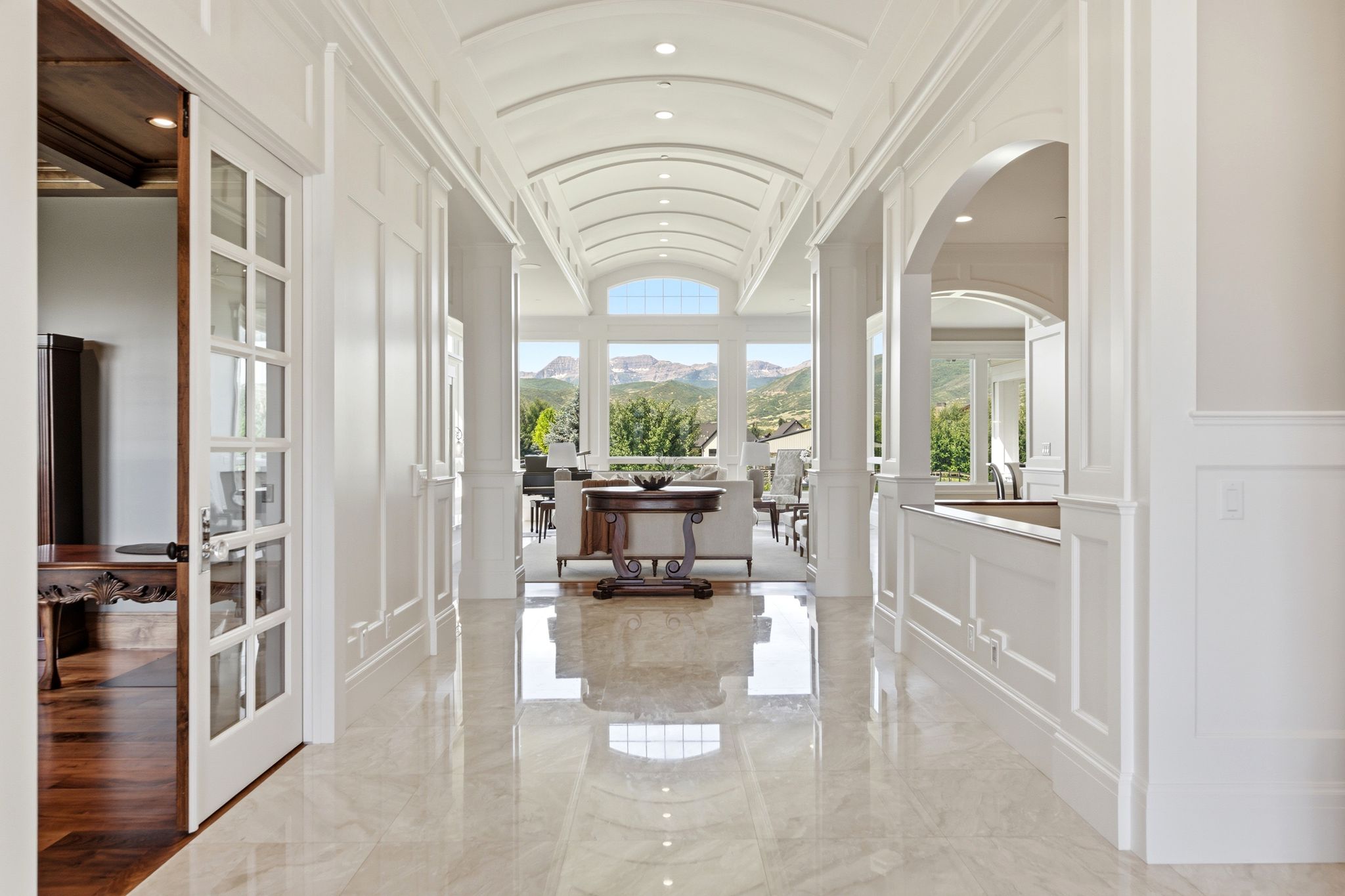 White wainscoting and polished stone flooring define this interior hallway, featuring a barrel-vaulted ceiling with recessed lighting