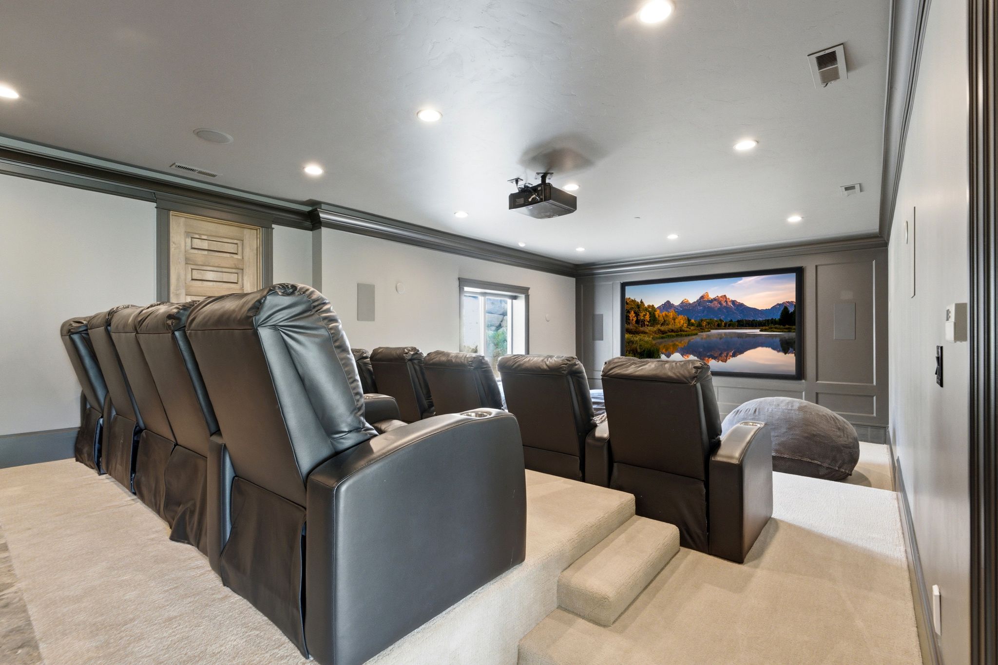 Dedicated media room featuring tiered seating, recessed lighting, crown molding, a large projection screen, and a ceiling-mounted projector