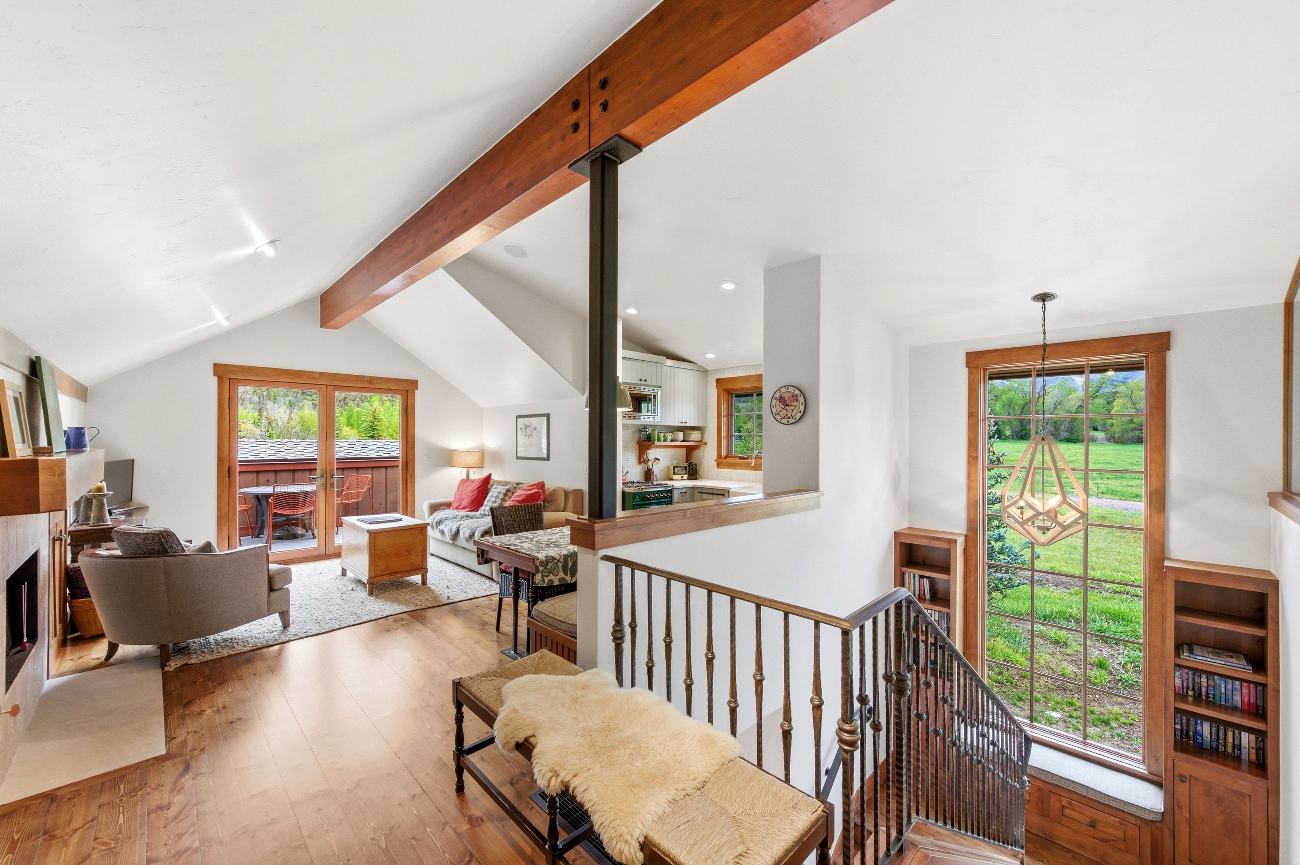 Vaulted ceilings with exposed wood beams, wood-finish flooring, and a stone fireplace
