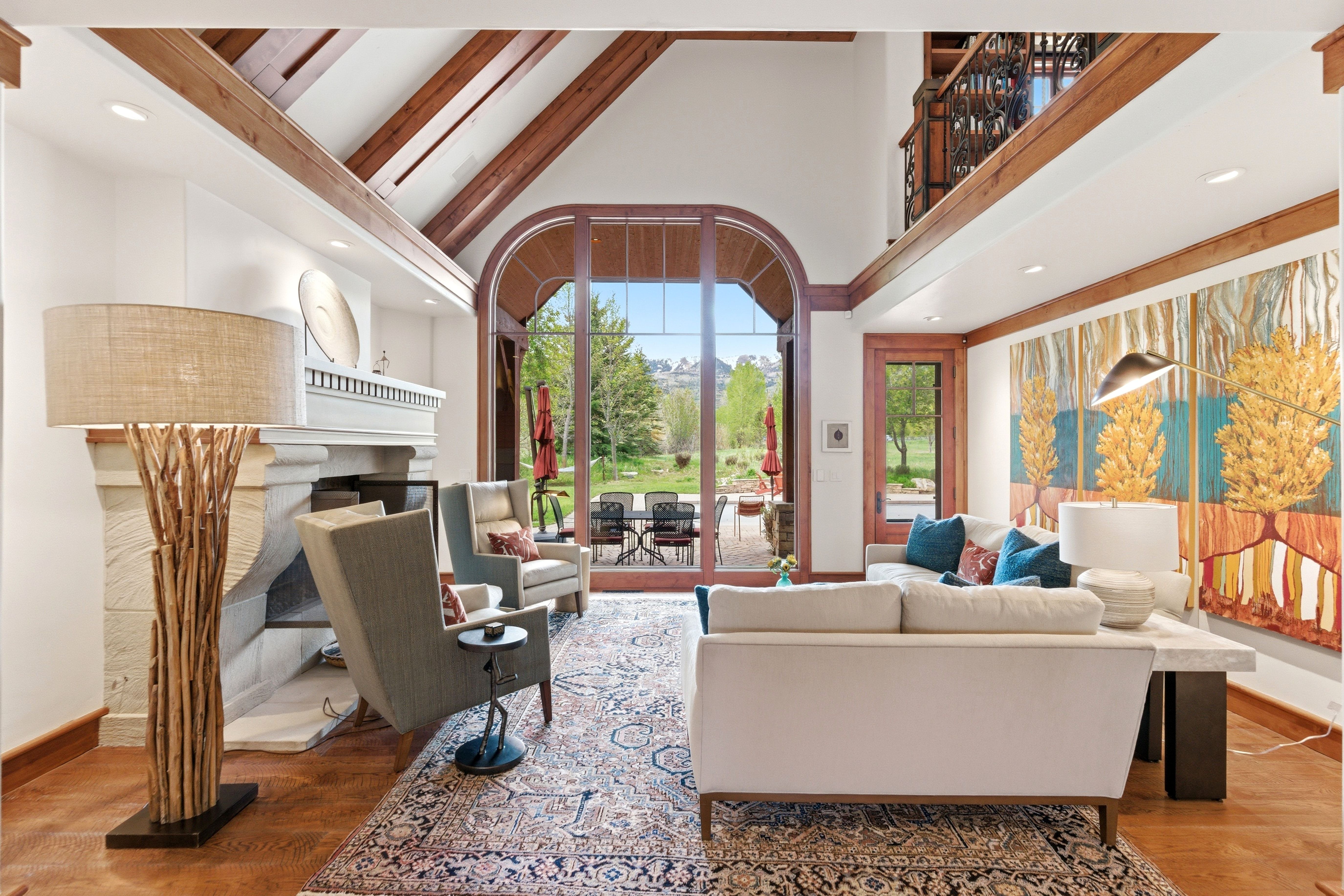 Spacious living area featuring high vaulted ceilings with exposed wood beams, a stone fireplace, and large arched glass doors