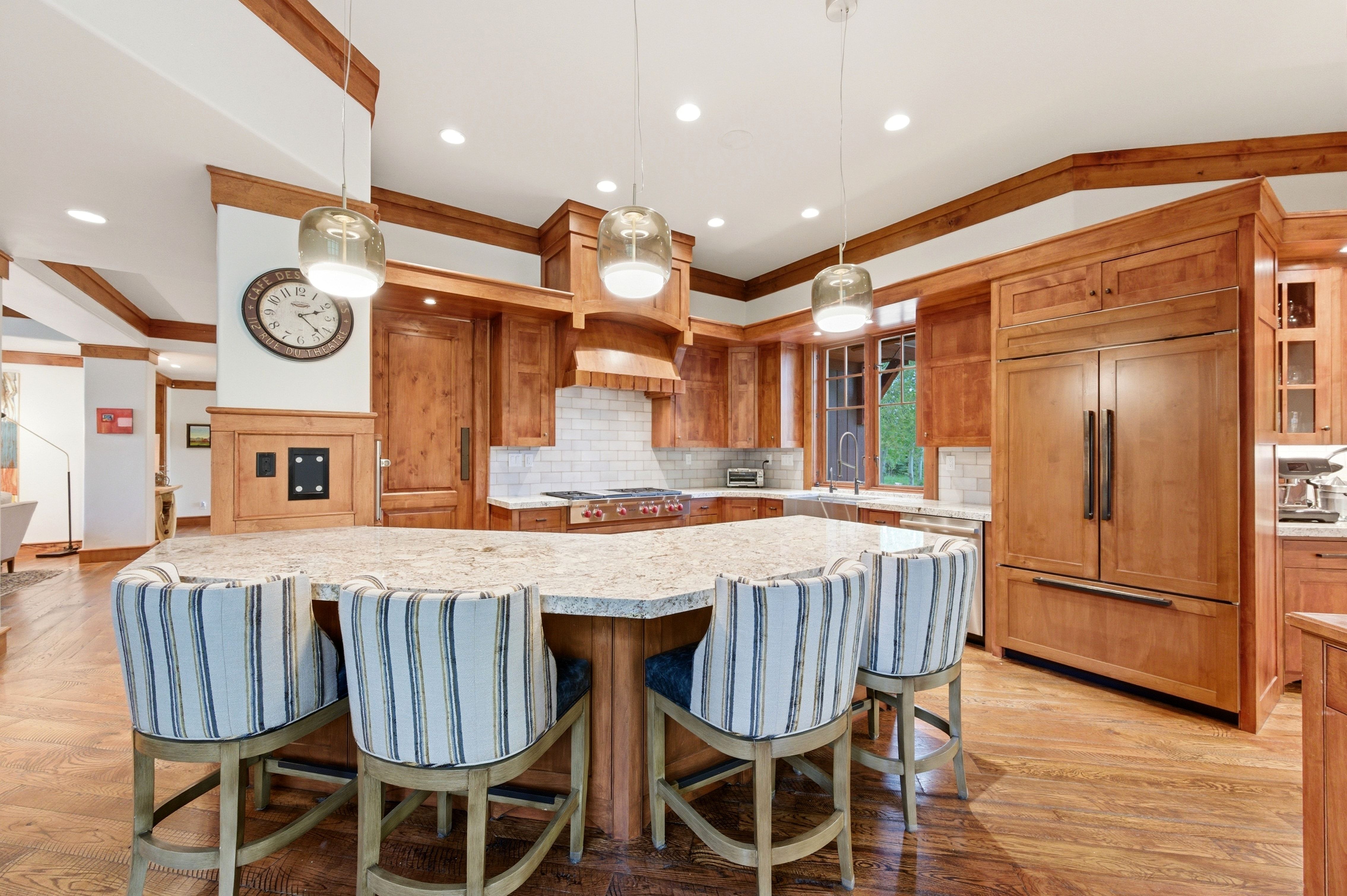 Gourmet kitchen featuring a large central island with light-toned countertop, rich wood cabinetry, integrated paneled refrigerator, white subway tile backsplash, and recessed lighting