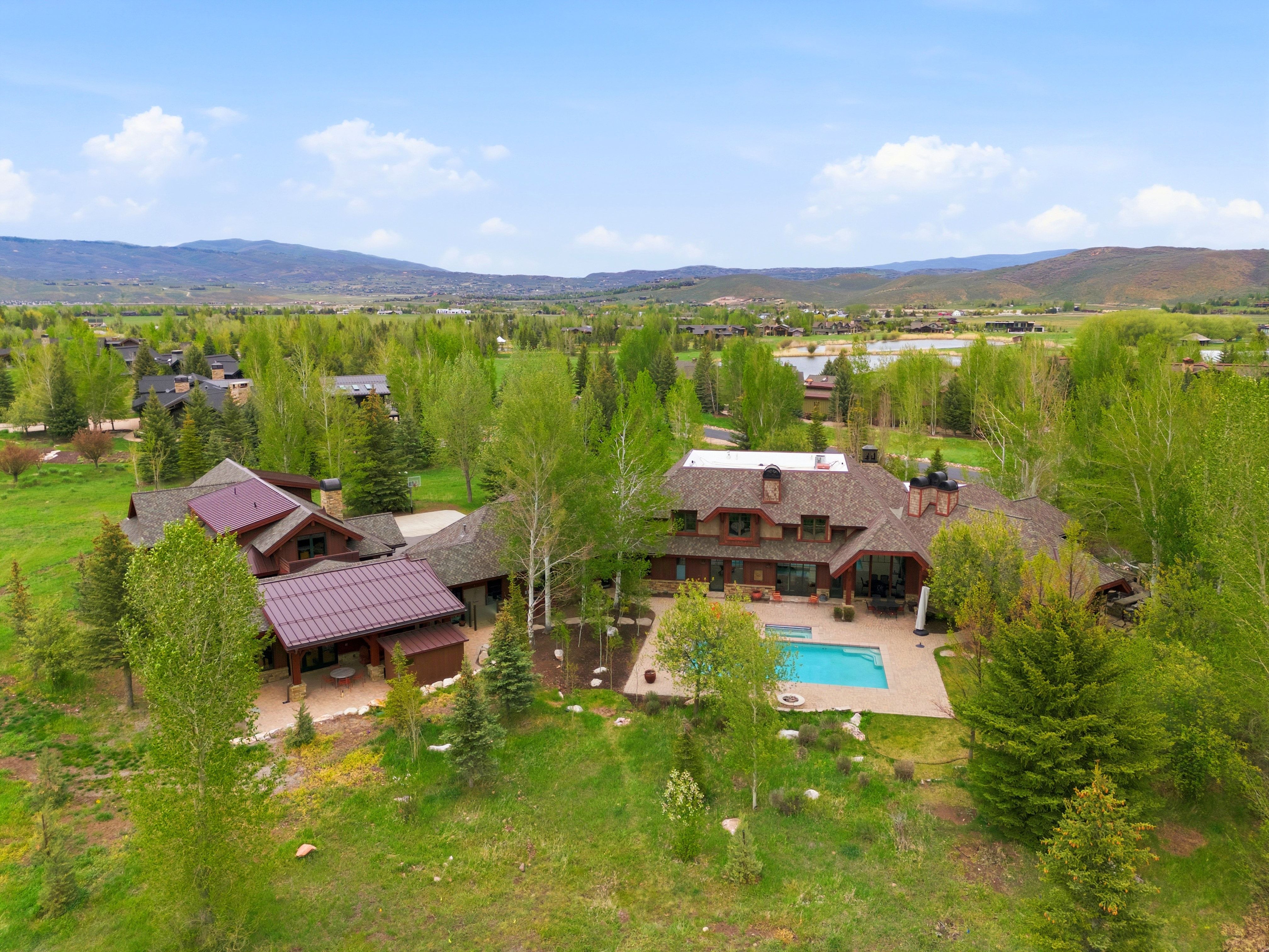 Expansive property featuring a multi-level residence with varied roofing materials, an outdoor pool, and surrounding mature trees