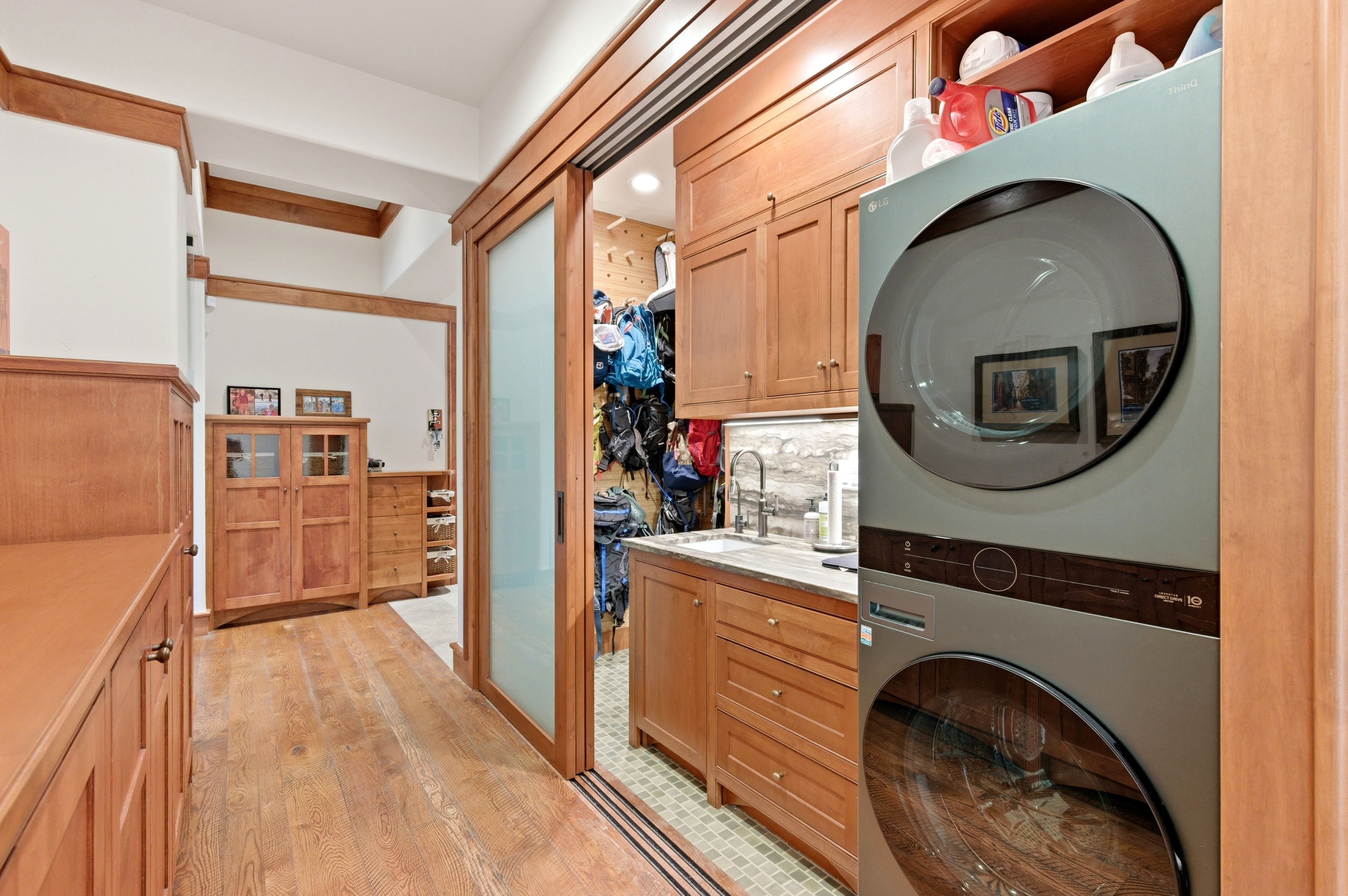 Dedicated laundry area featuring a stacked washer and dryer unit, ample built-in cabinetry, a utility sink, and wood-finish flooring