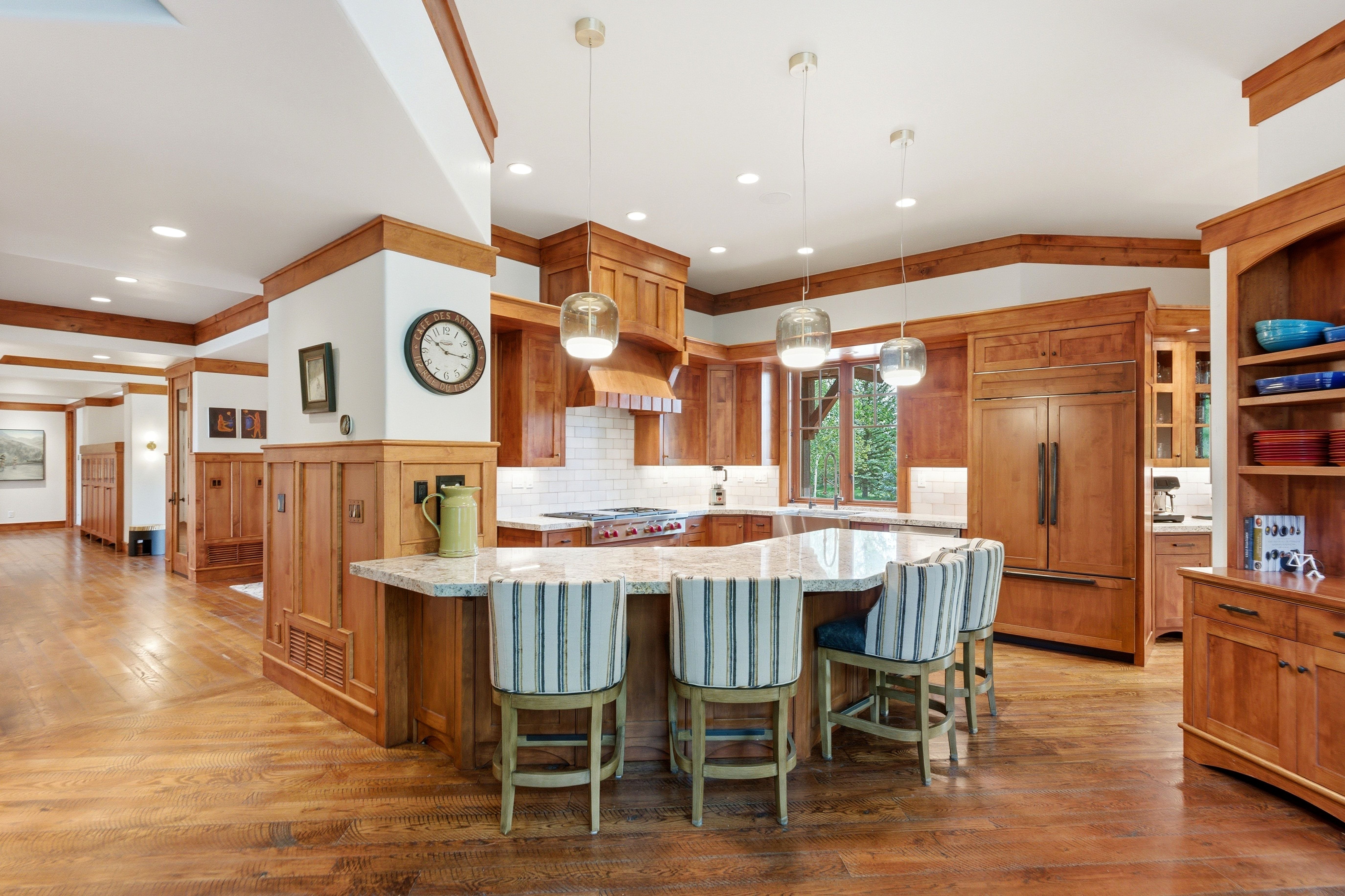 Gourmet kitchen featuring a large stone-top island, integrated panel appliances, custom wood cabinetry, subway tile backsplash, and wood-finish flooring