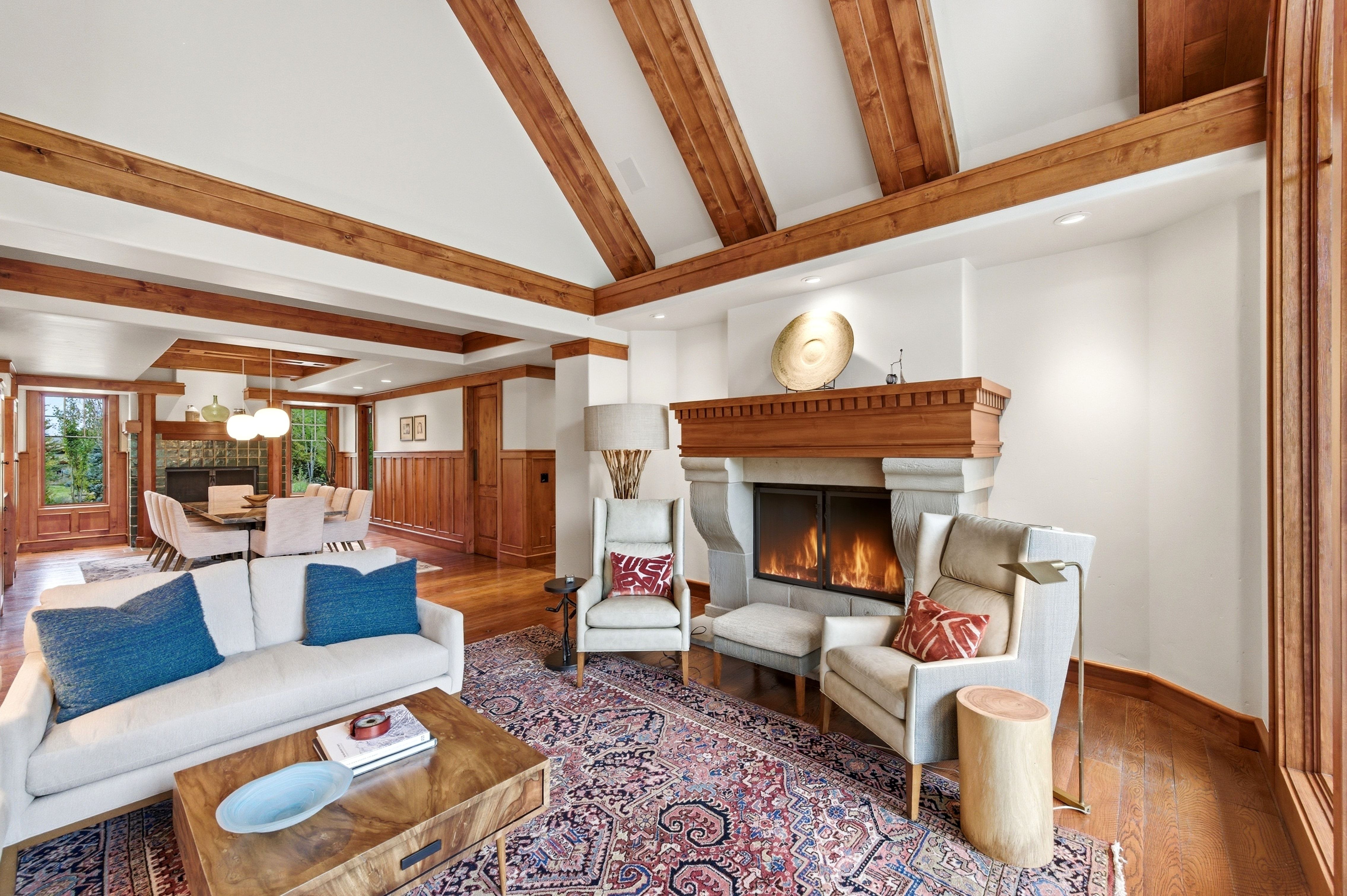 Living area featuring a stone fireplace with a wood mantel, exposed wood ceiling beams, and wood-finish flooring