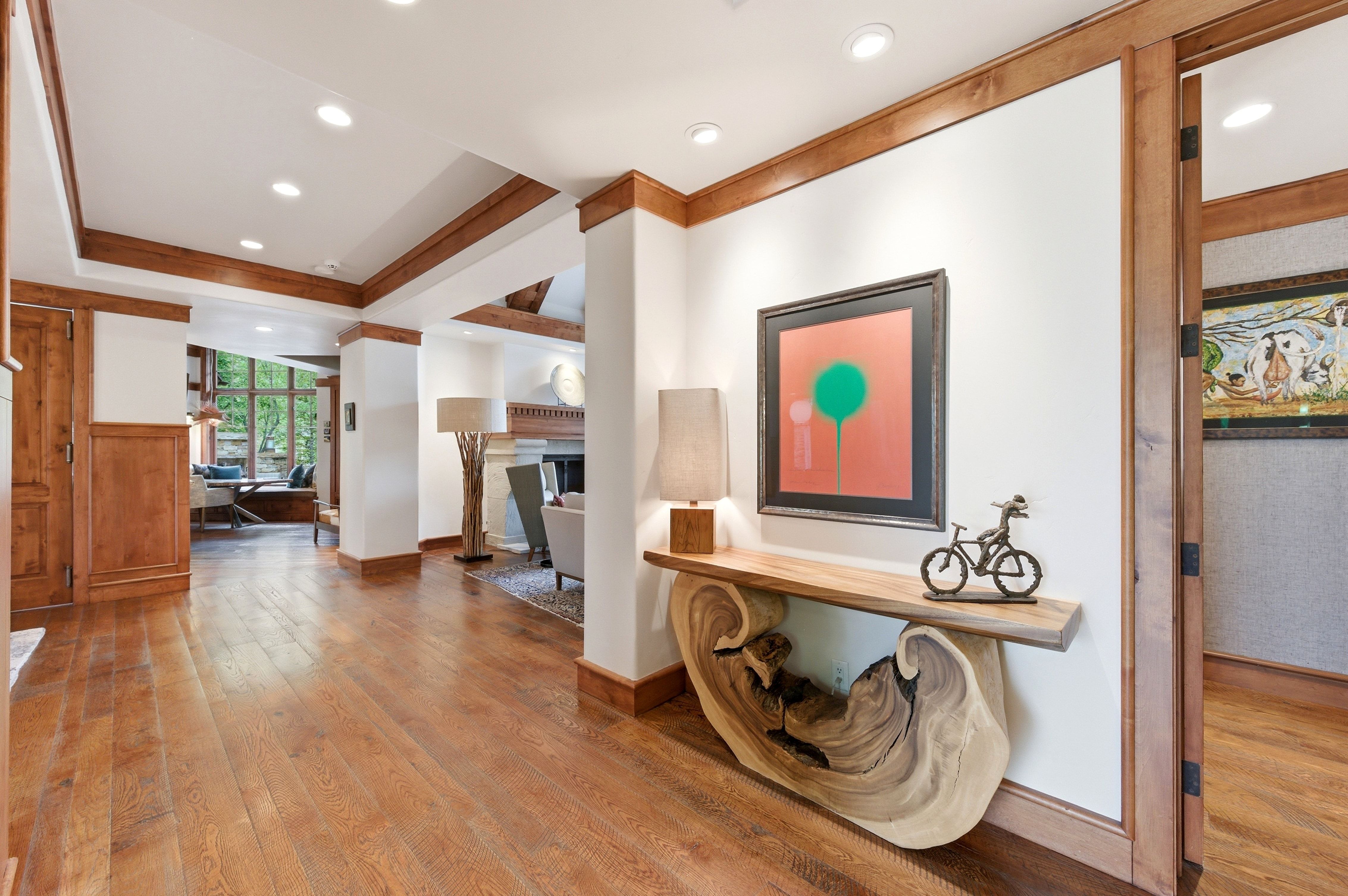 Spacious interior entry featuring wood-finish flooring, recessed lighting, white walls with wood wainscoting, and a decorative console table with a live-edge base