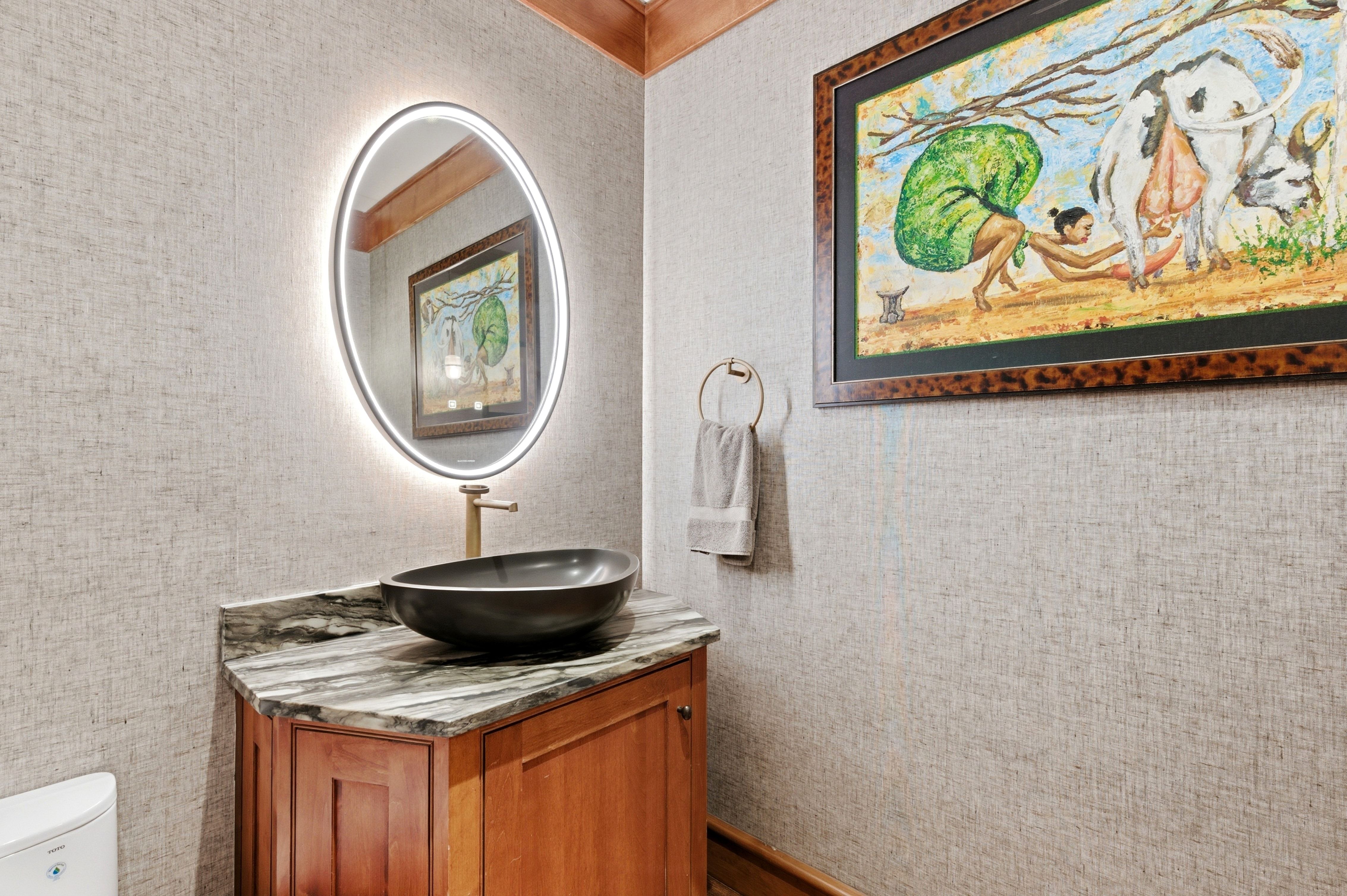 Powder room featuring a wood vanity with a stone countertop, vessel sink, and backlit oval mirror
