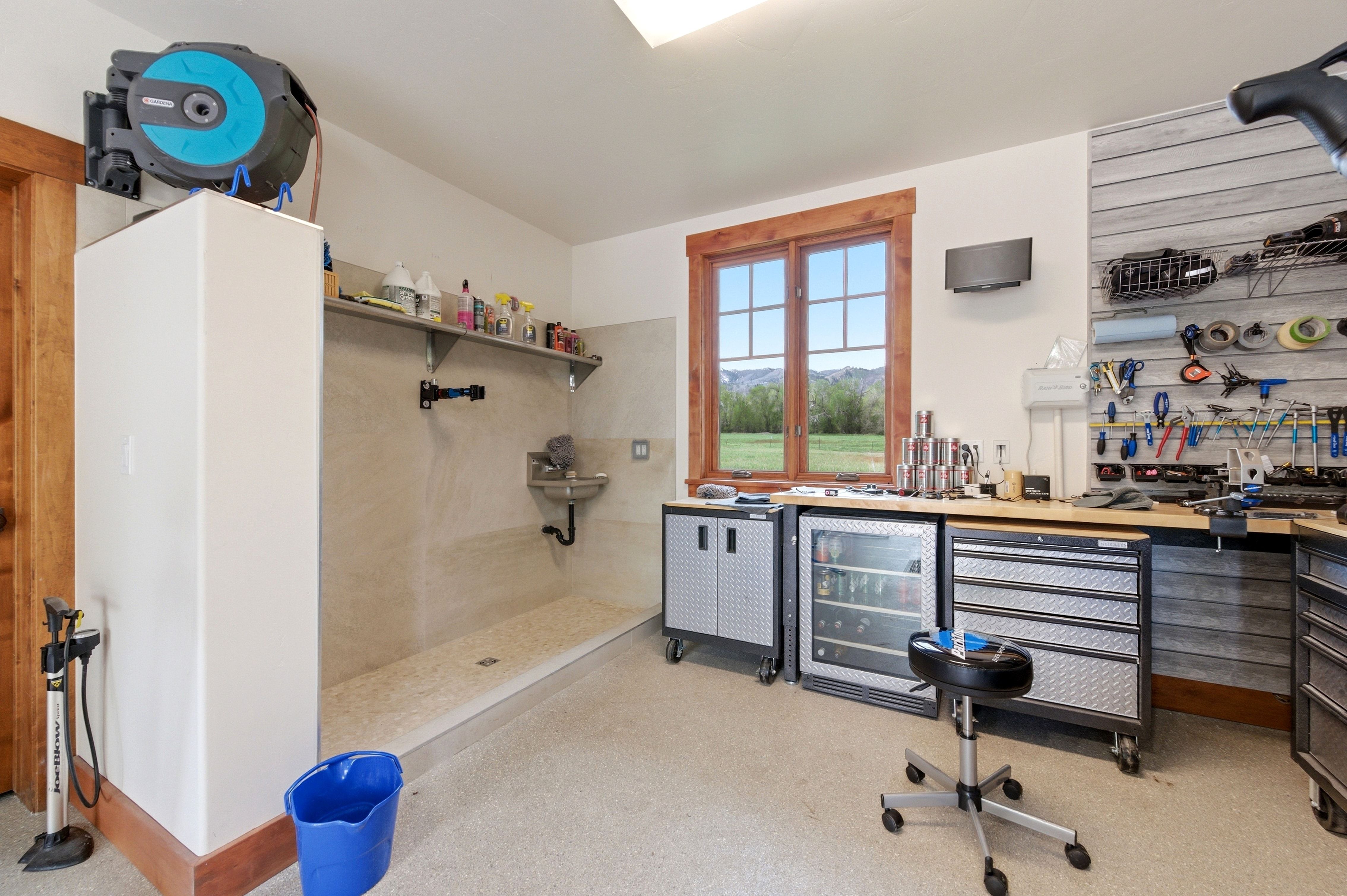 Functional utility room featuring a built-in wash station with tiled walls and floor, a wood-trimmed window, extensive workbench space, and integrated storage solutions