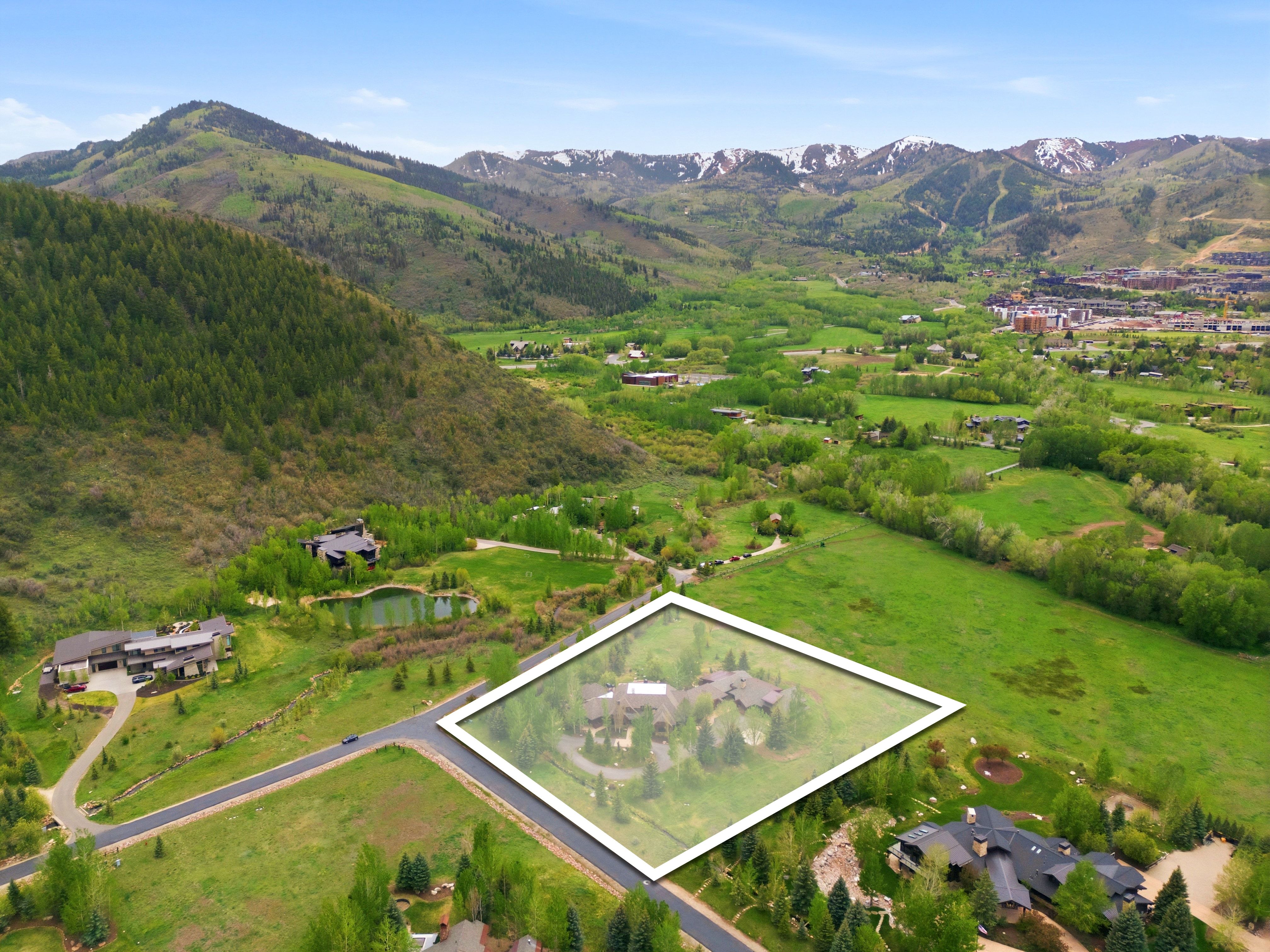 Aerial perspective showcasing a sprawling property with extensive green space, a curved driveway, and mature landscaping