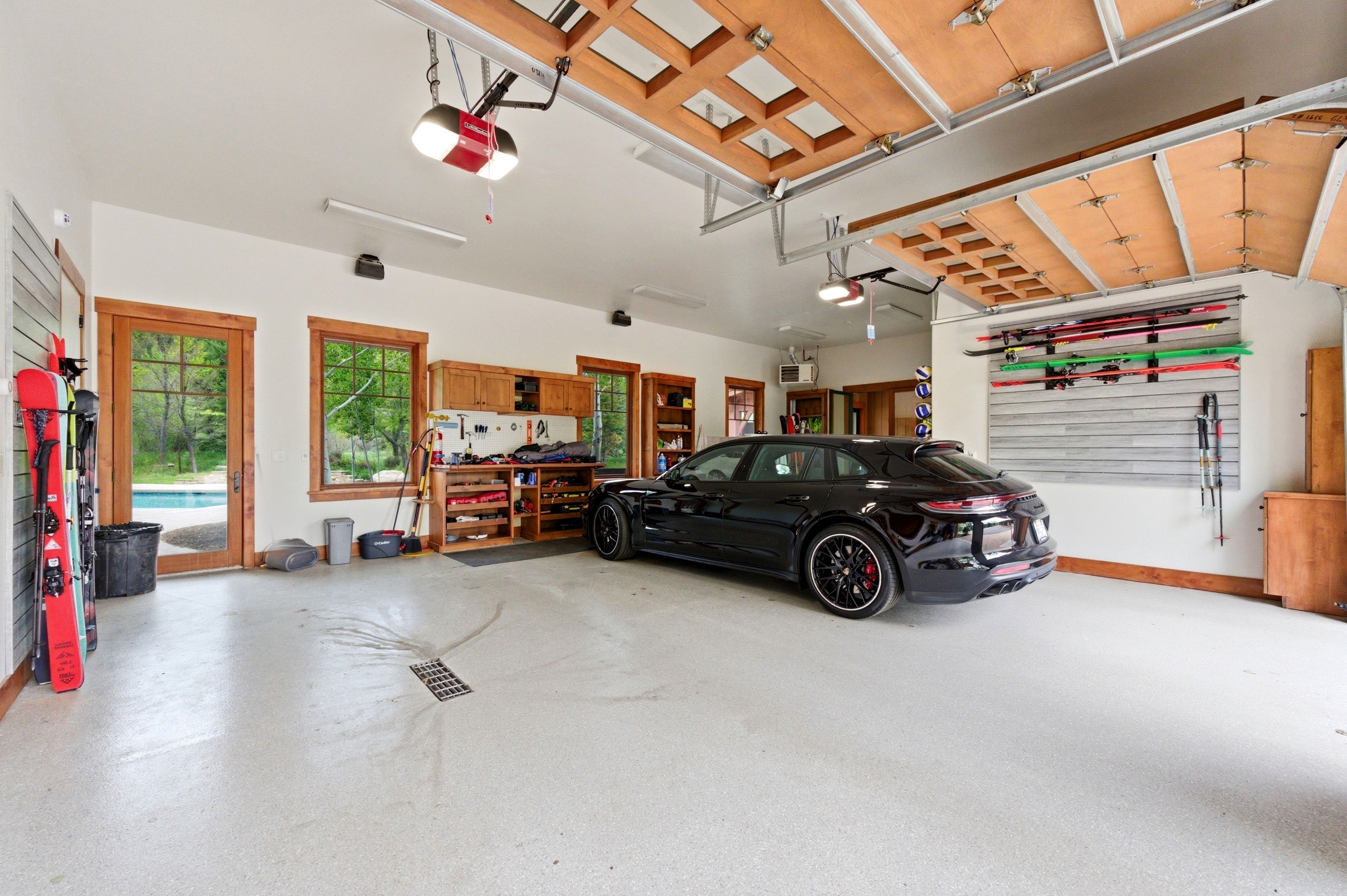 Spacious garage featuring light-toned epoxy flooring, a built-in workbench with storage, natural wood window and door frames, and a glass-paned exterior door