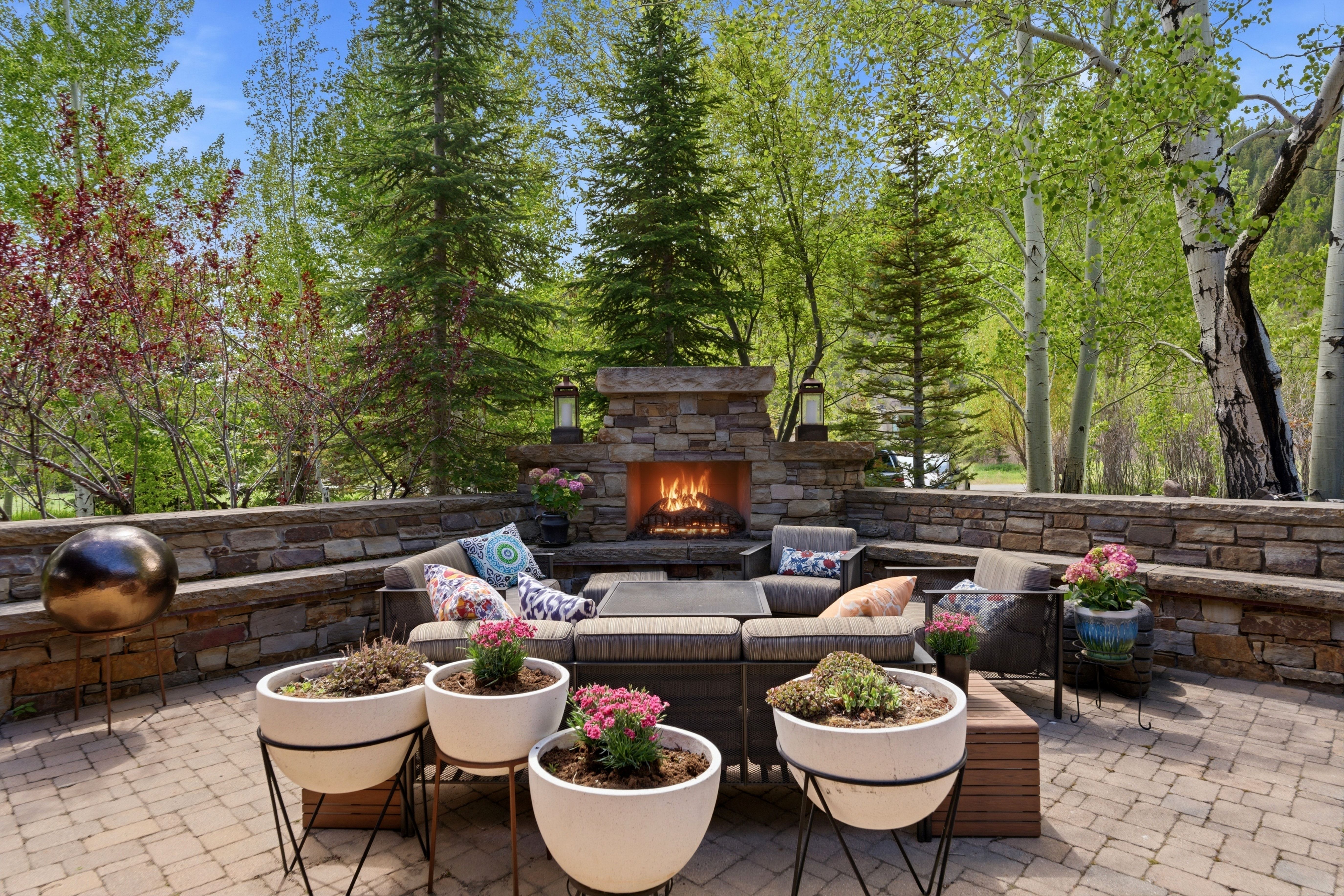 Spacious paver patio with a built-in stone fireplace, stone seating, and a stone retaining wall