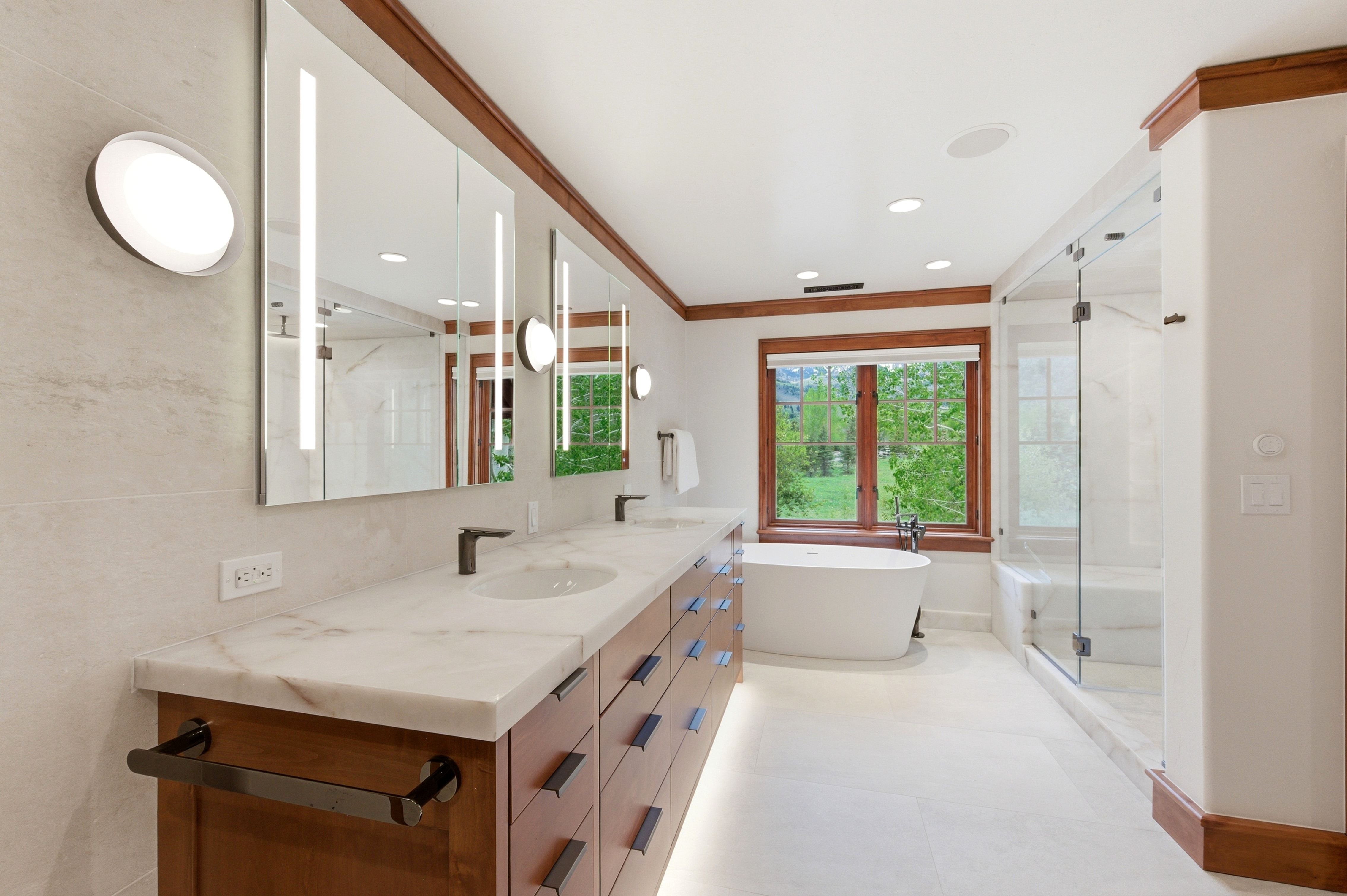 Dual vanity with a stone countertop and undermount sinks, featuring integrated illuminated mirrors and modern wall sconces