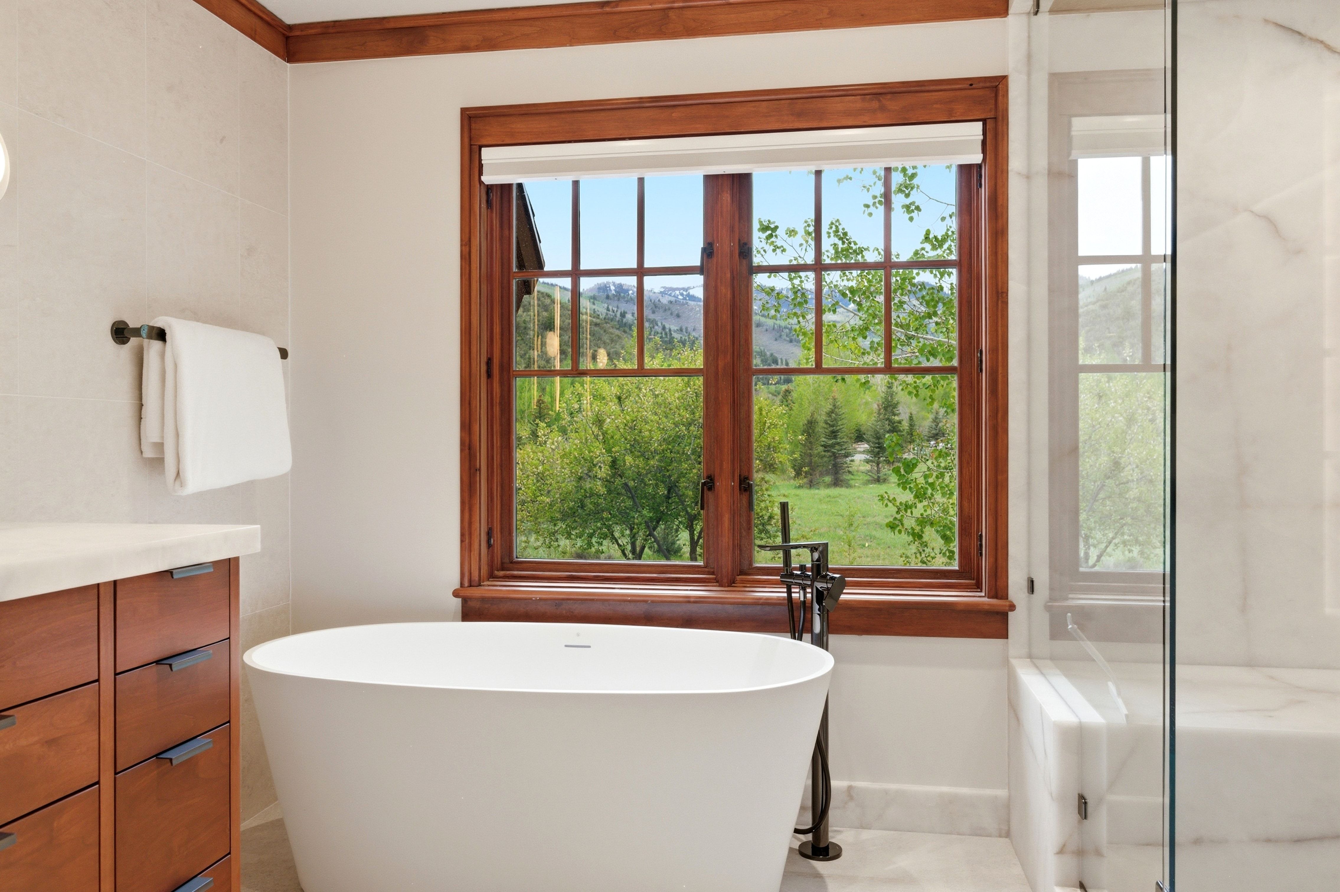 Freestanding soaking tub with a floor-mounted faucet positioned before a large window with wood trim