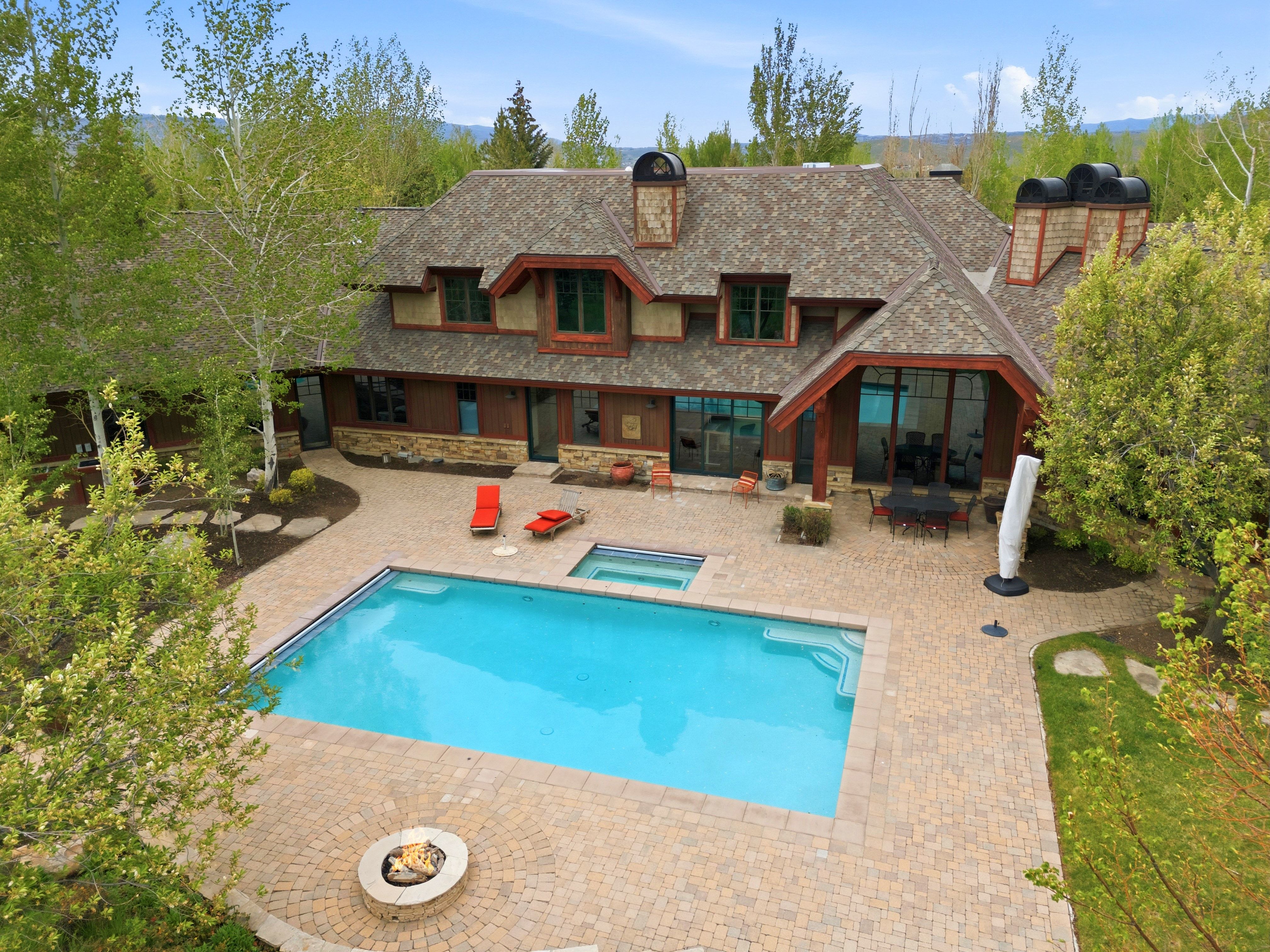 Expansive paver patio featuring a rectangular swimming pool, integrated spa, and a circular fire pit