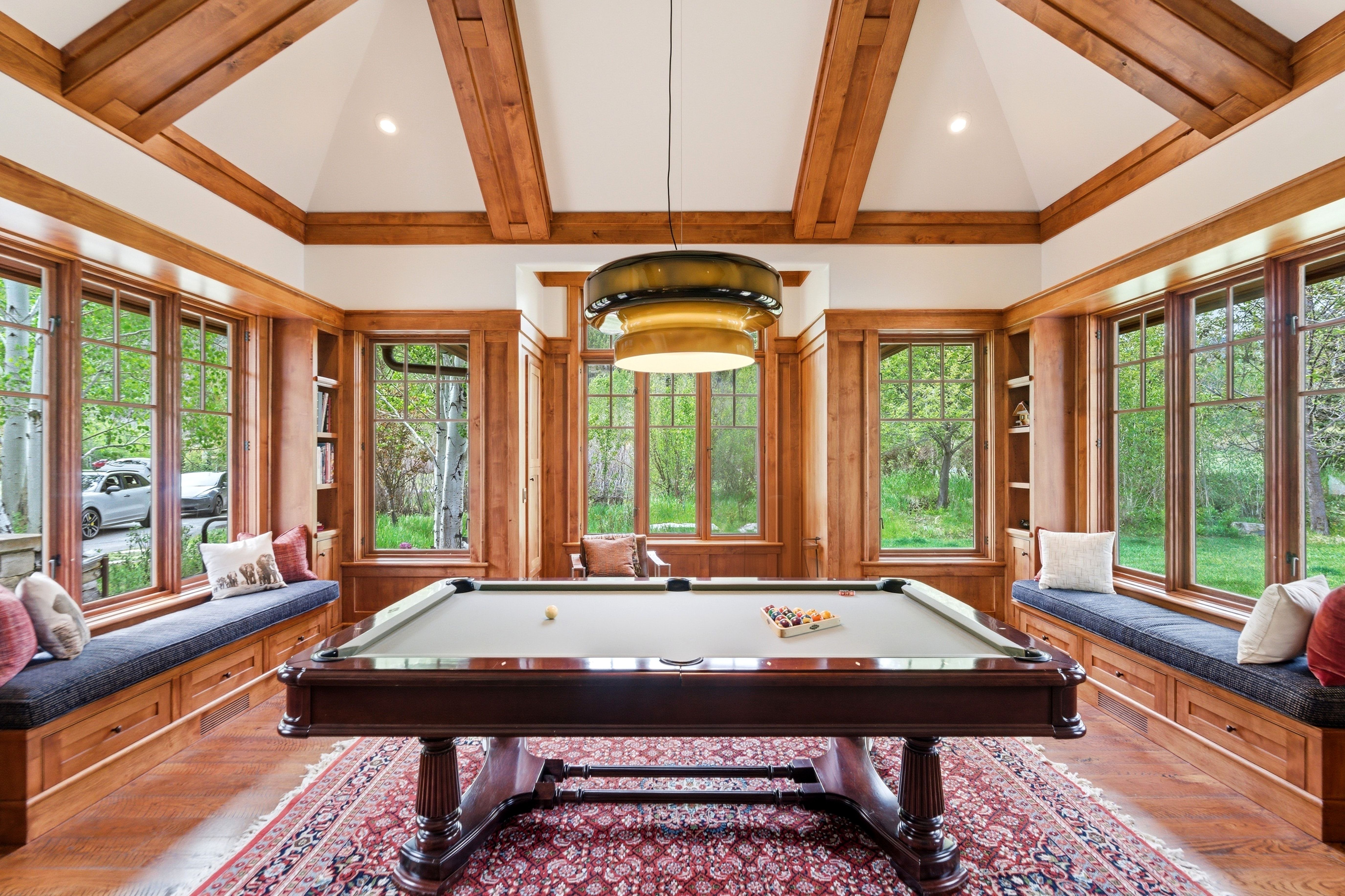 Spacious recreation room featuring a vaulted ceiling with exposed wood beams, extensive wood-finish window trim, and integrated window seating with storage